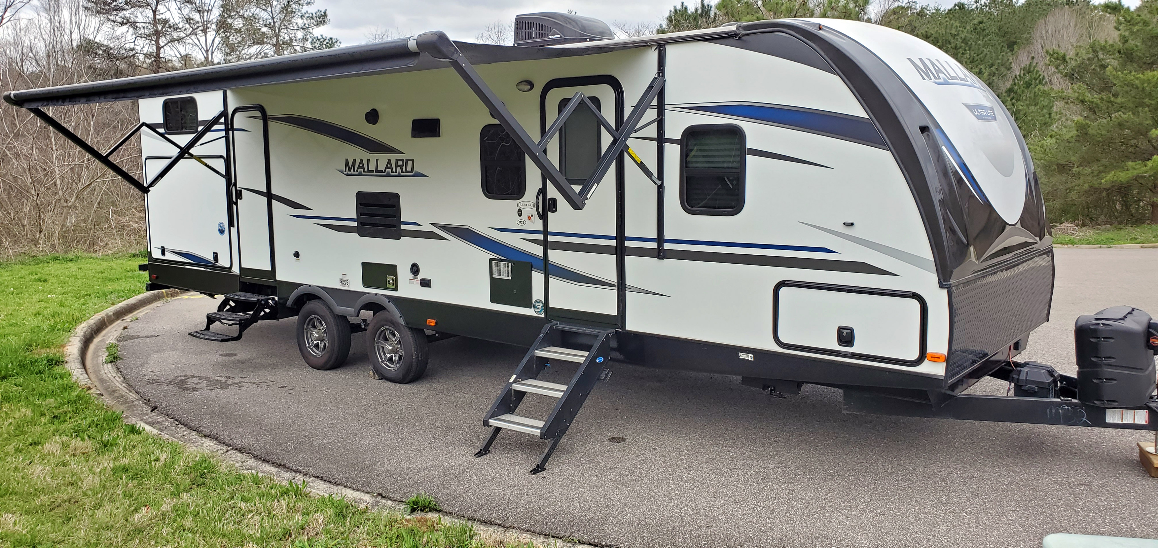 This white Mallard travel trailer, perfect for an RV rental, is parked with its awning extended and steps deployed.. Heartland RVs Mallard 2021