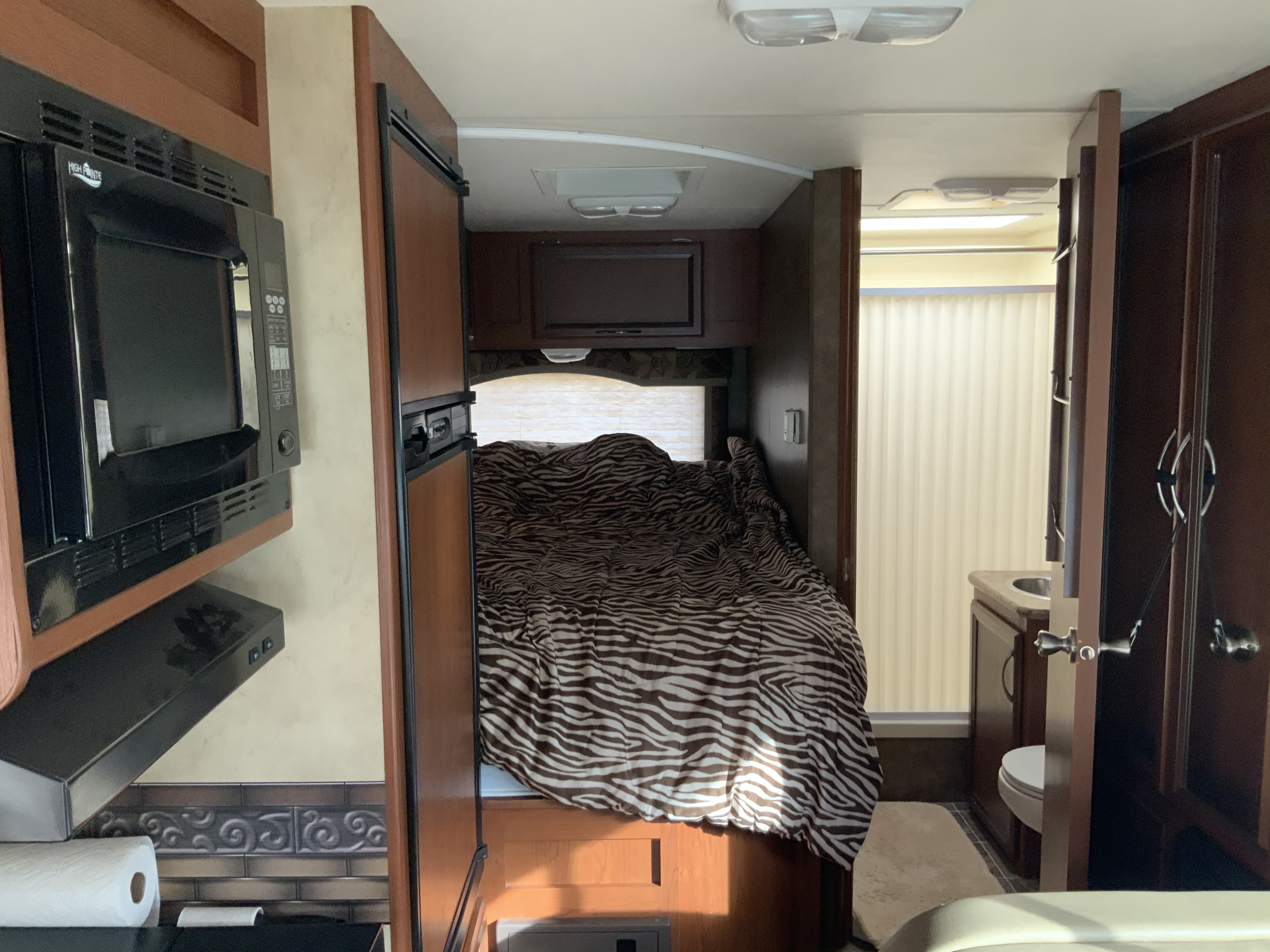 This RV rental's interior shows a compact kitchen, cozy bedroom with a zebra comforter, and functional bathroom setup.. Thor Motor Coach Four Winds 2013