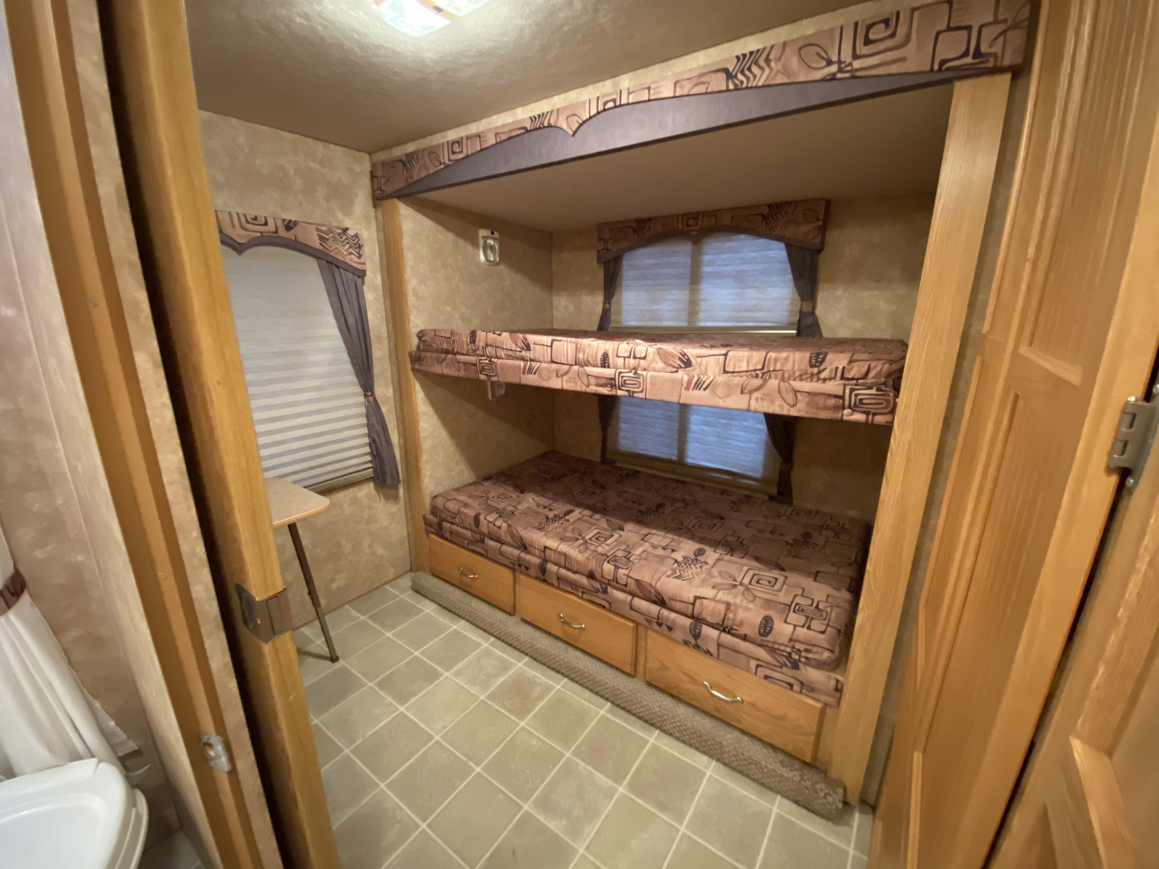 This RV rental features a cozy interior with two bunk beds, patterned mattresses, under-bed drawers, and window blinds. Ideal for family camping.. Okanagan Eclipse 2005