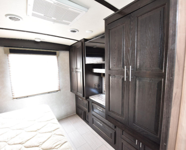 RV rental bedroom featuring dark wood cabinets, a comfy bed, & bright window. Plenty of storage for your travels.. Forest River FR3 30DS 2020