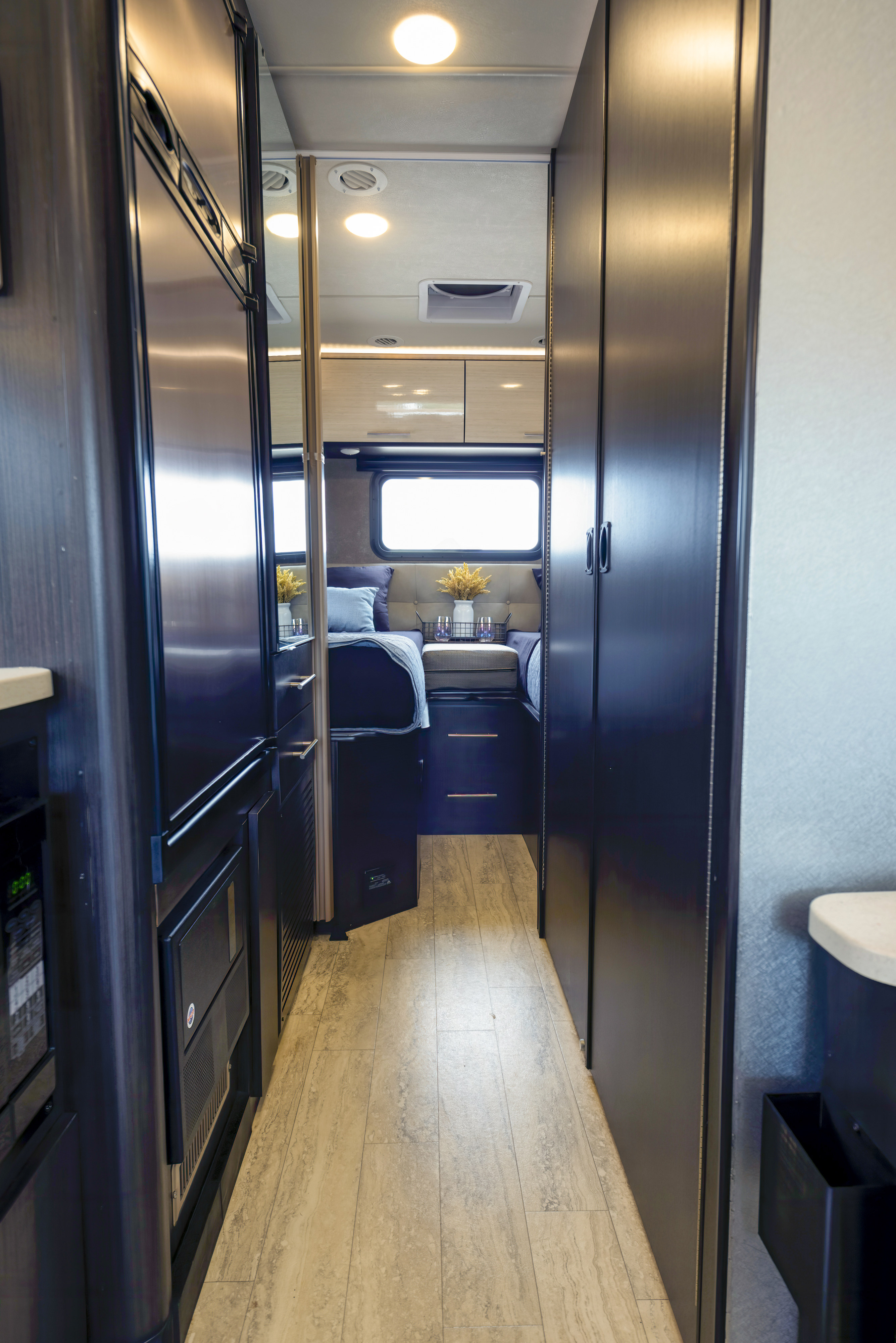 A sleek hallway inside a modern RV rental, leading to a cozy bedroom with twin beds and bright window.. Thor Motor Coach Axis 2018