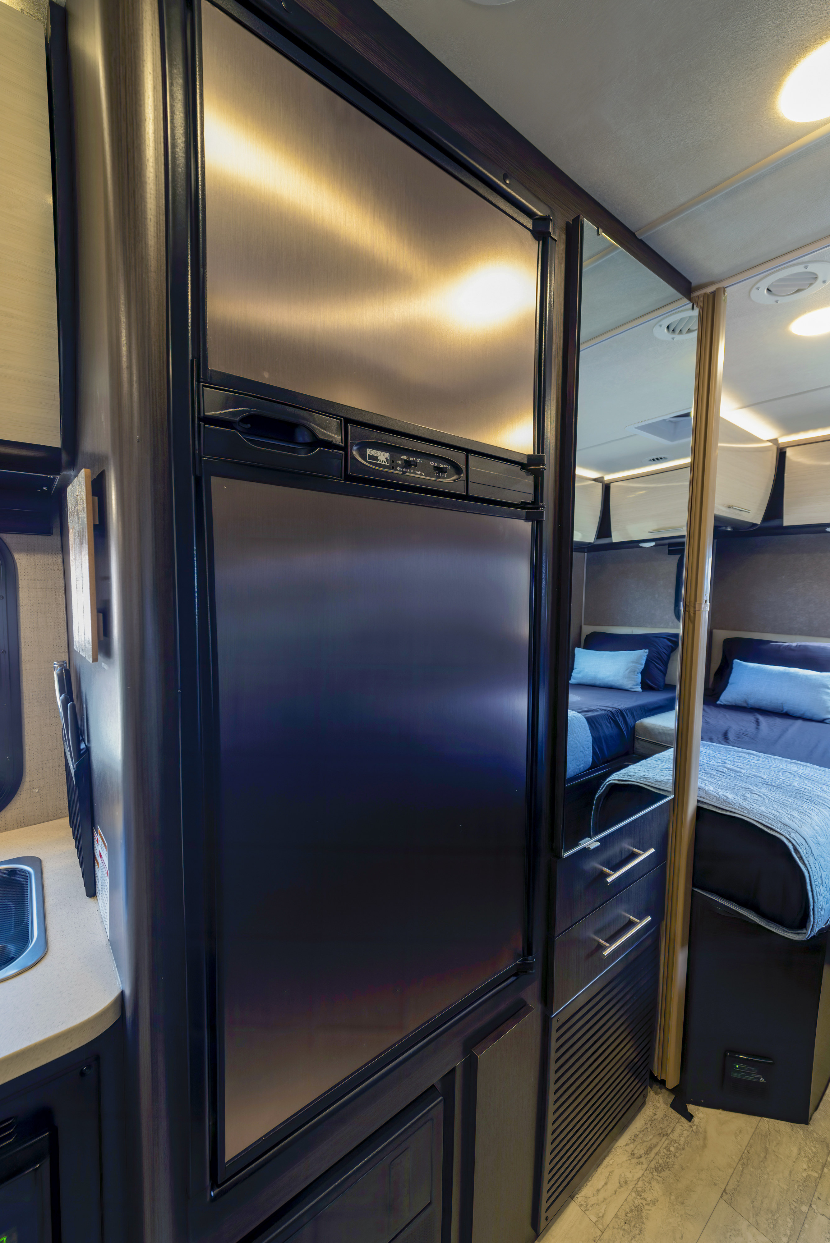 Inside an RV rental: a sleek stainless steel refrigerator stands beside a full-length mirror reflecting the cozy bedroom.. Thor Motor Coach Axis 2018