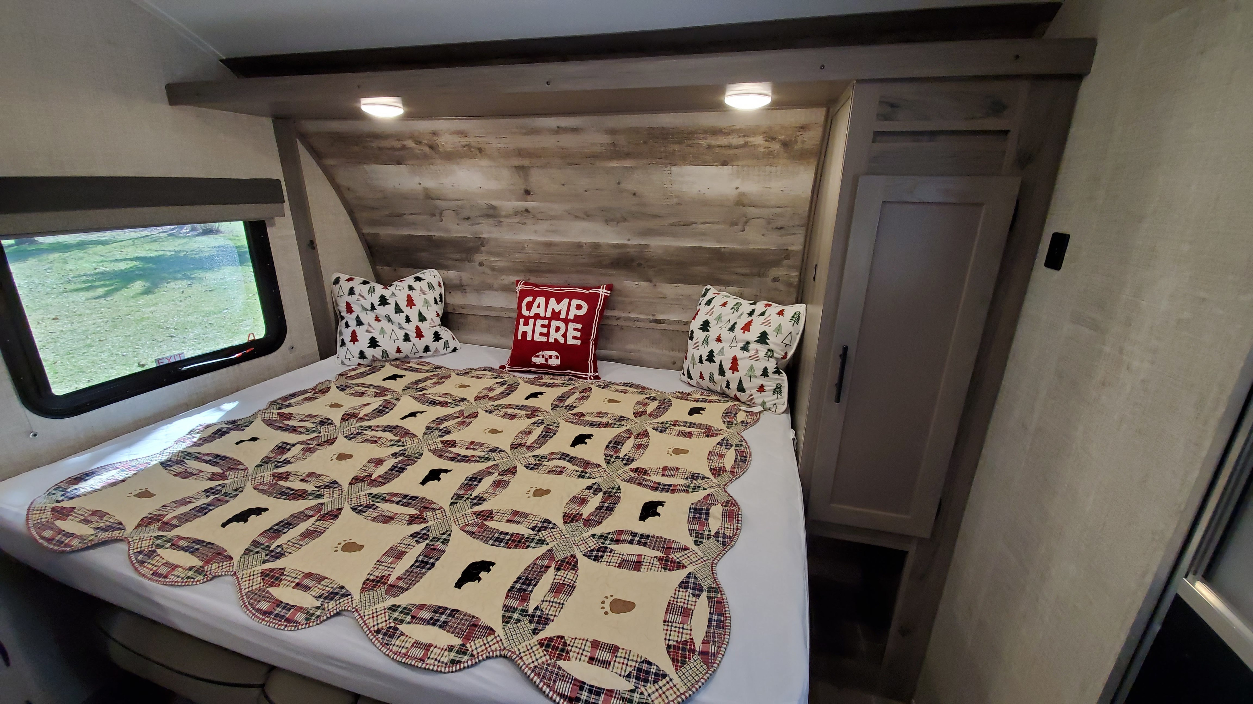 Cozy RV rental bedroom with a rustic quilt featuring bears, themed pillows, and a scenic window view.. Gulf Stream Ameri-Lite 2021