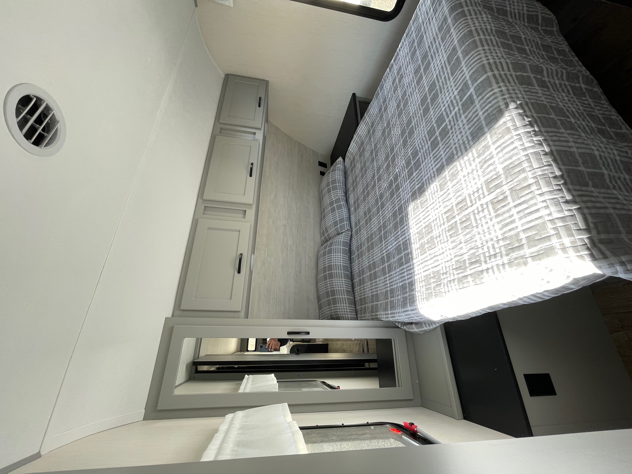 Inside an RV rental: a modern, compact bedroom with a plaid bed, overhead cabinets, and integrated storage below.. Forest River Vibe 2021