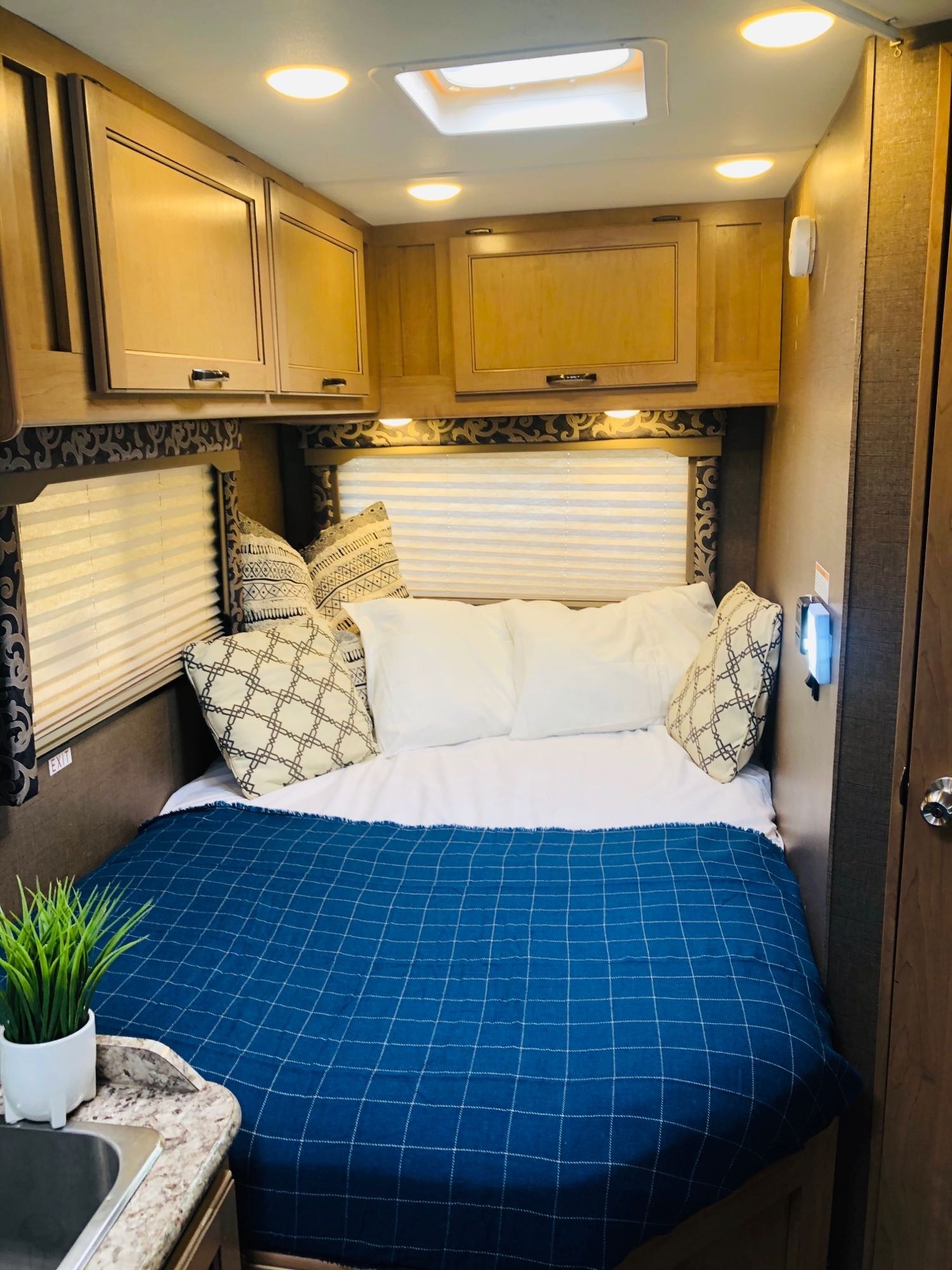 Cozy RV rental bedroom with a comfy bed, blue blanket, overhead cabinets, and bright interior lighting.. Thor Four Winds 2019