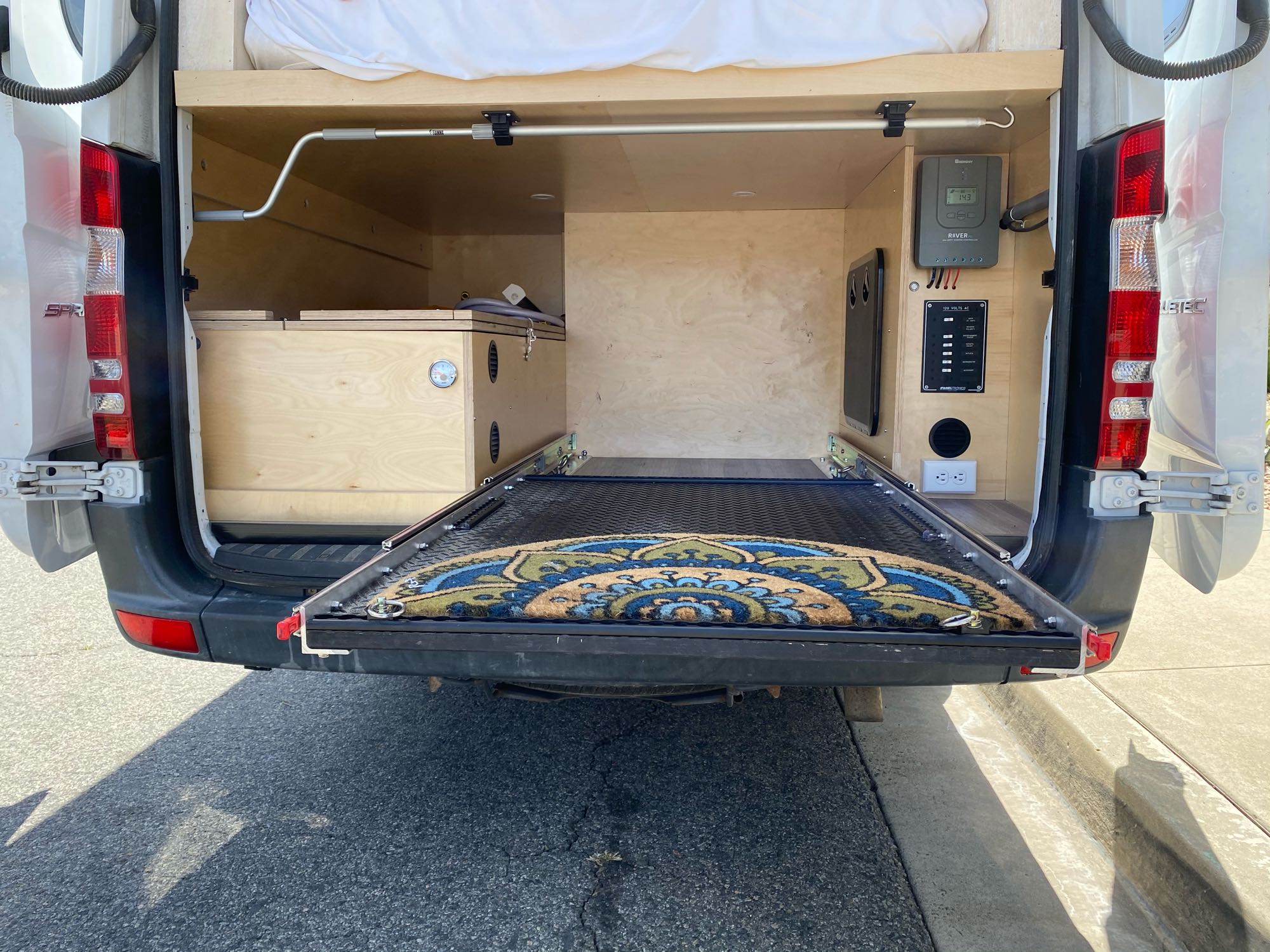 RV rental camper van interior with rear doors open, showing custom bed, pull-out storage, and power panel.. Mercedes-Benz Sprinter 2014