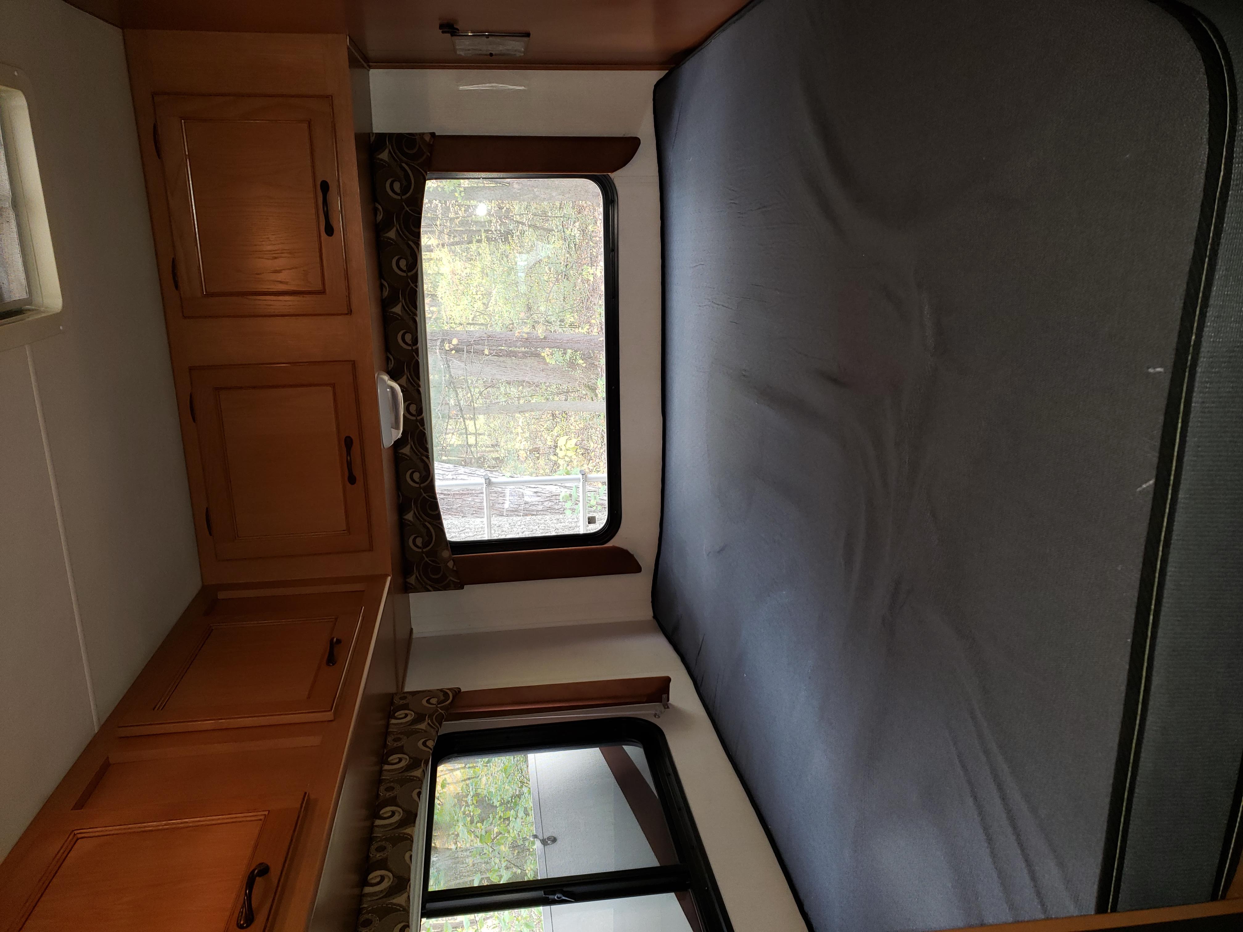 Inside a spacious RV rental: comfortable sleeping area, ample wood cabinets, and large windows revealing a nature view.. Coachmen Freelander 2013