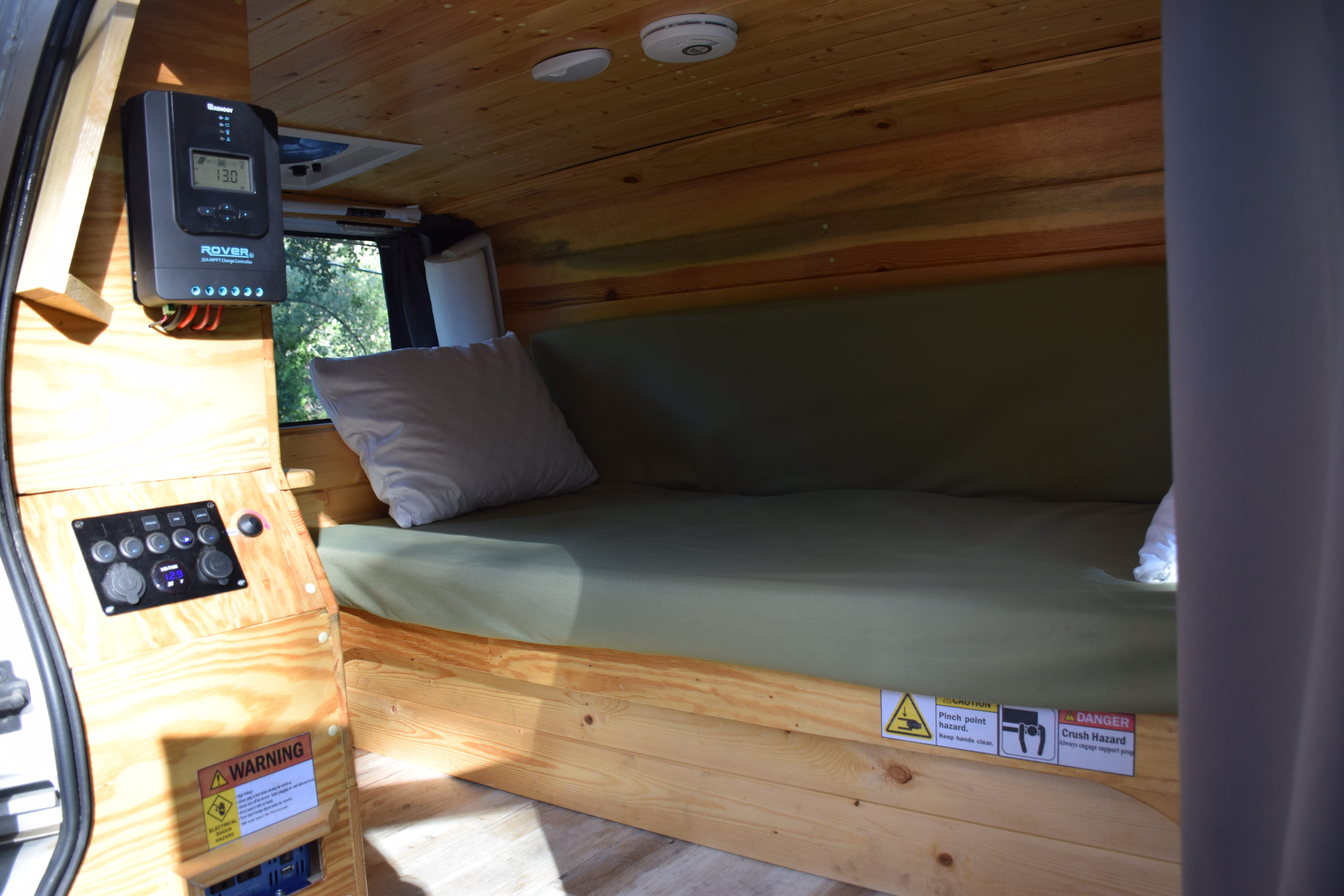 RV rental interior: custom wooden build with bed, solar charge controller, and electrical panel featuring 12.9V display.. Other Other 2000
