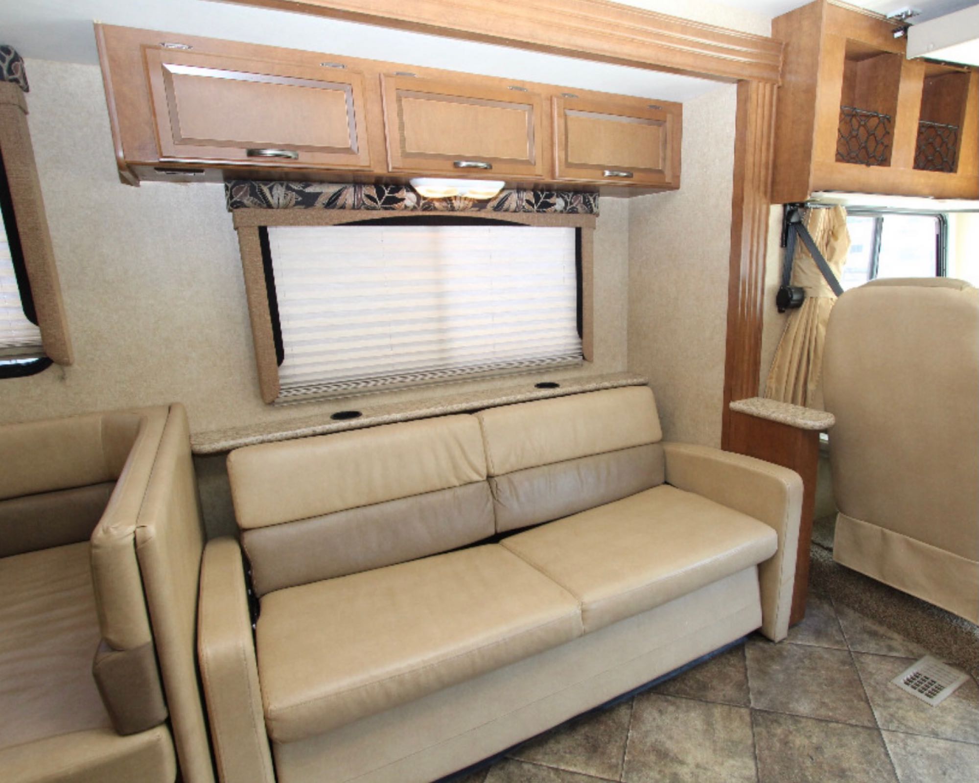 This RV rental features a cozy living area with a beige sofa, overhead wooden cabinets, and large windows with blinds, on a tiled floor.. Other A.C.E 2014