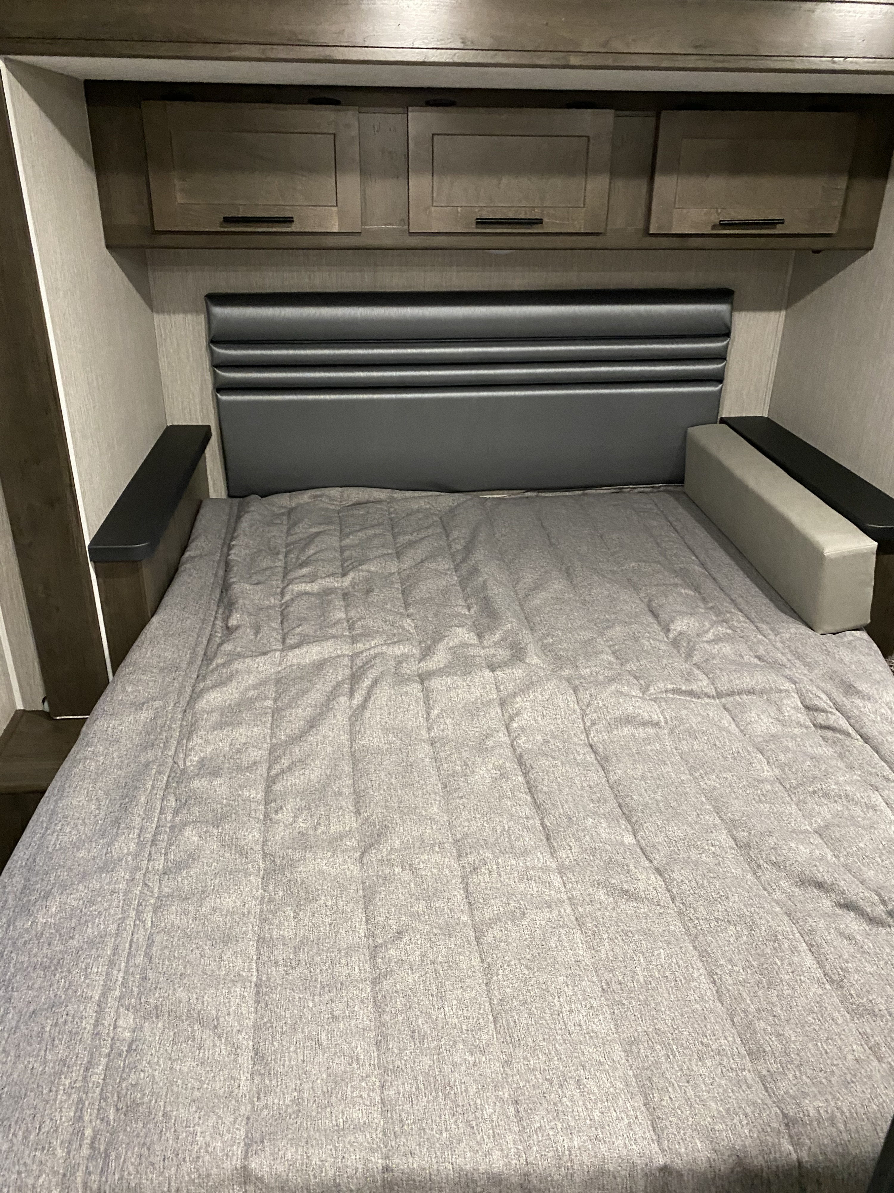 Comfortable RV rental bedroom with a gray bed, padded headboard, and overhead storage cabinets.. Coachmen Leprechaun 311 fs 2021