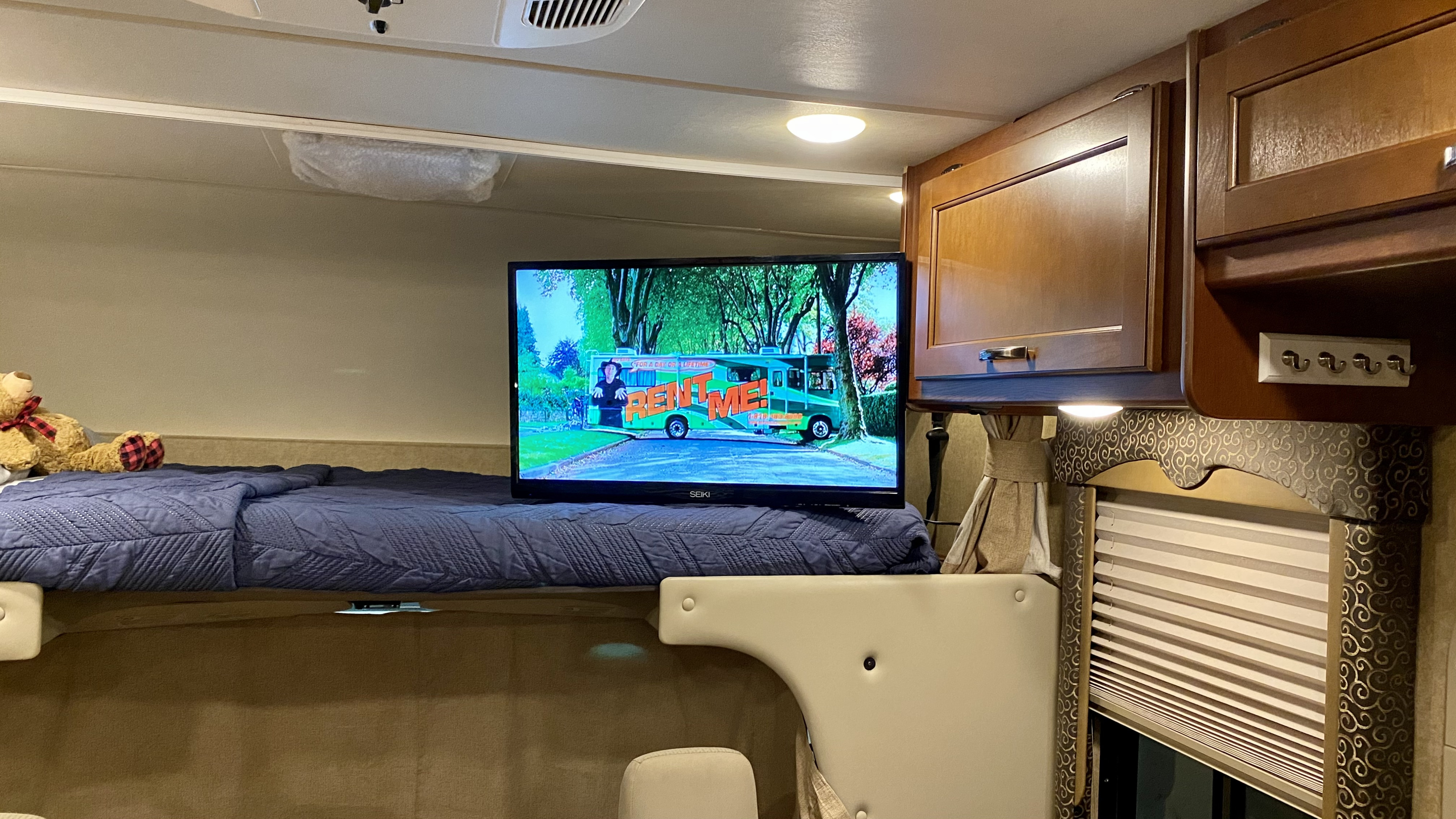 Cozy RV bunk bed area with a teddy bear and TV displaying an RV rental ad, perfect for trips.. Thor Motor Coach Freedom Elite 2017