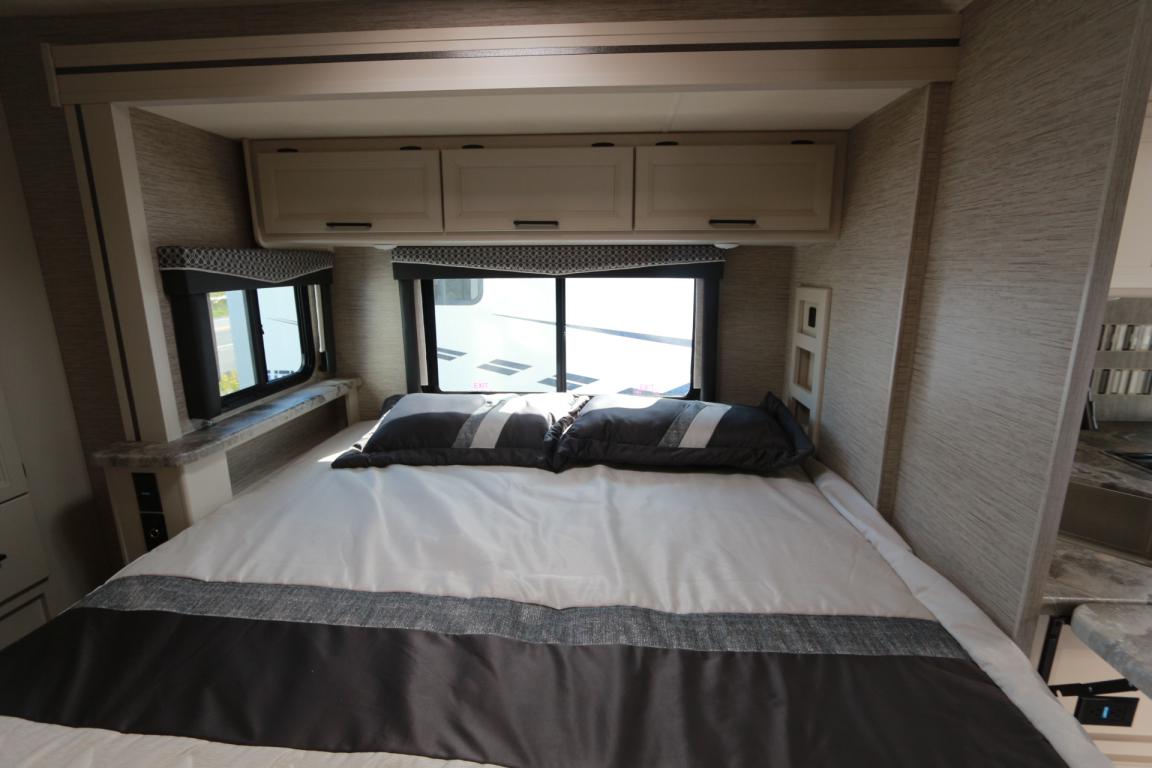 Comfortable RV rental bedroom featuring a large bed, overhead cabinets, and two windows for natural light.. Thor Chateau 2021