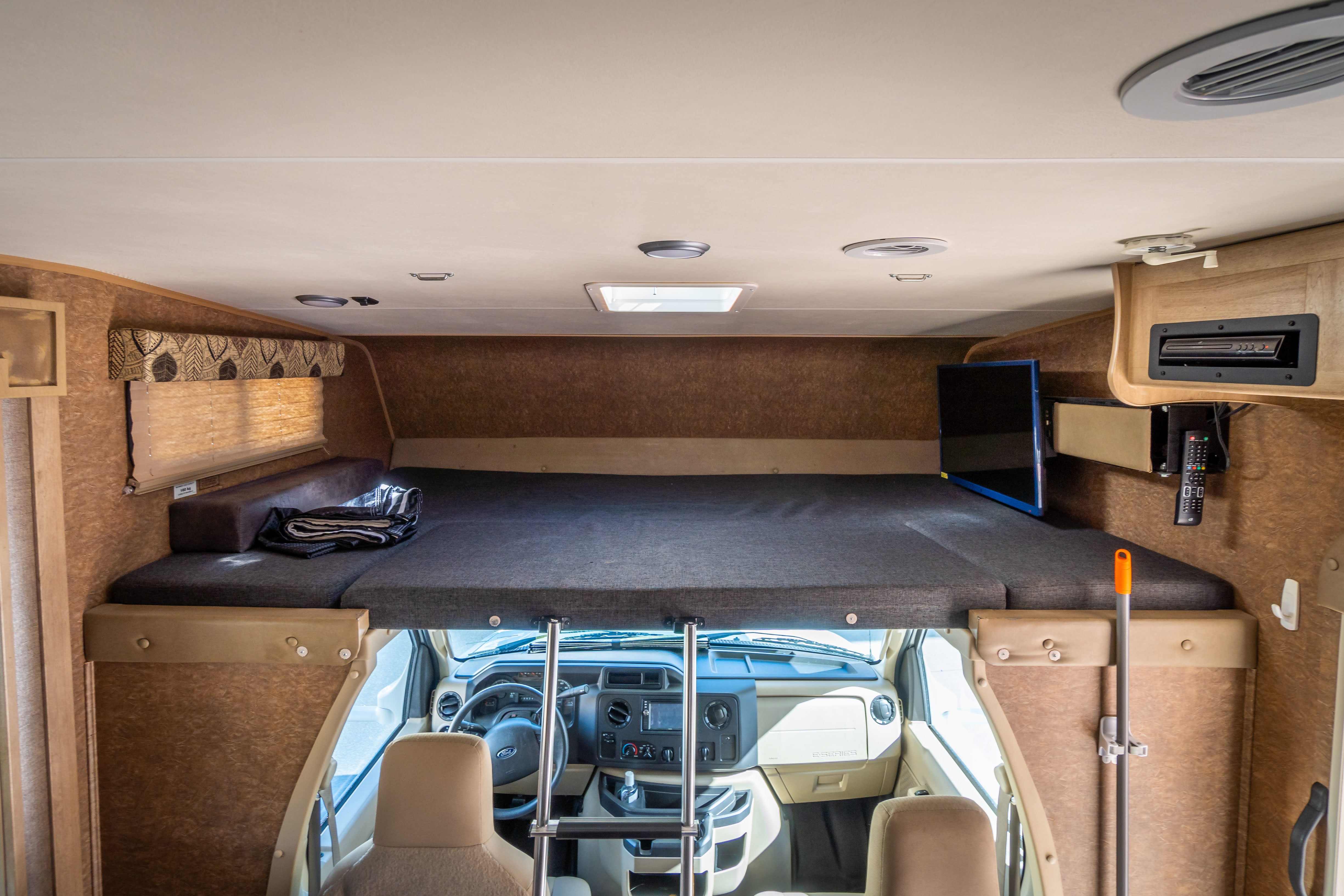 Interior view of an RV rental: a spacious cab-over bunk with a TV and access ladder, positioned above the driver's cockpit.. Forest River Coachmen Freelander 2016