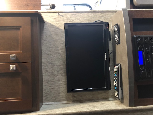 RV rental interior: wall-mounted TV, remote controls, and entertainment system beside a wood cabinet.. Forest River Sunseeker 2017