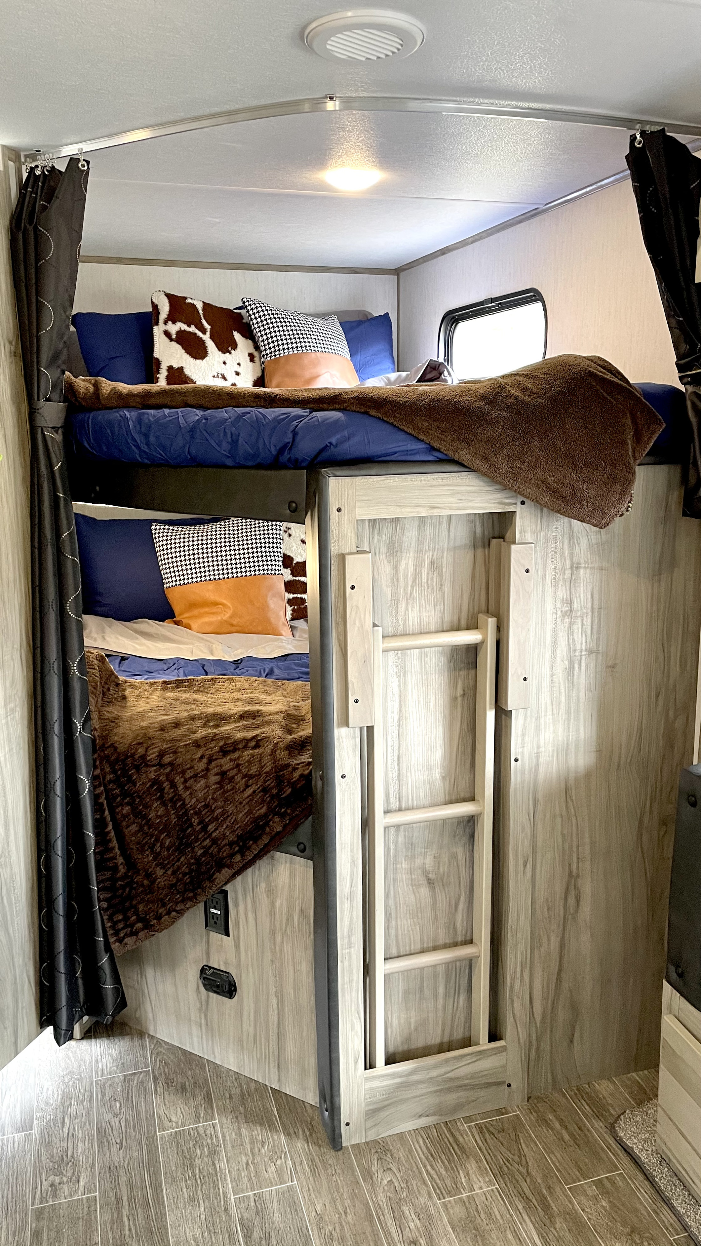 An RV rental's sleeping area features cozy bunk beds, complete with bedding, privacy curtains, and a ladder.. Forest River Cherokee 2021