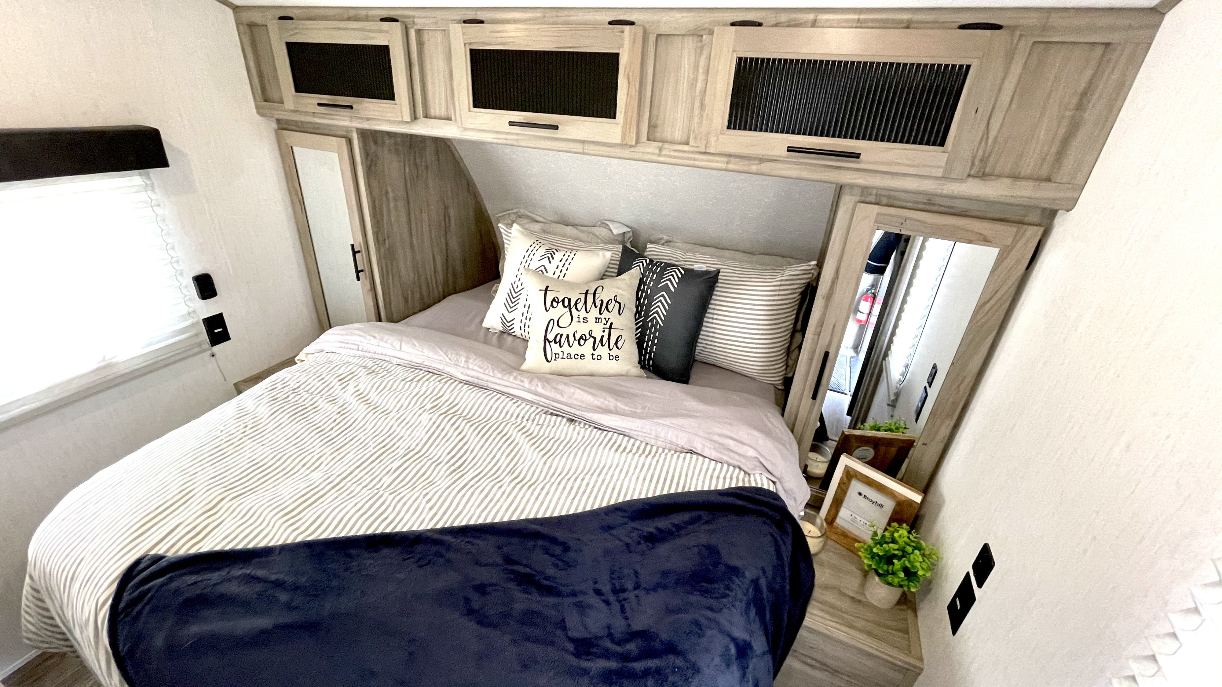 Cozy RV rental bedroom with striped bedding, overhead cabinets, decorative pillows, and mirrored accents. Ideal for a comfortable stay.. Forest River Cherokee 2021