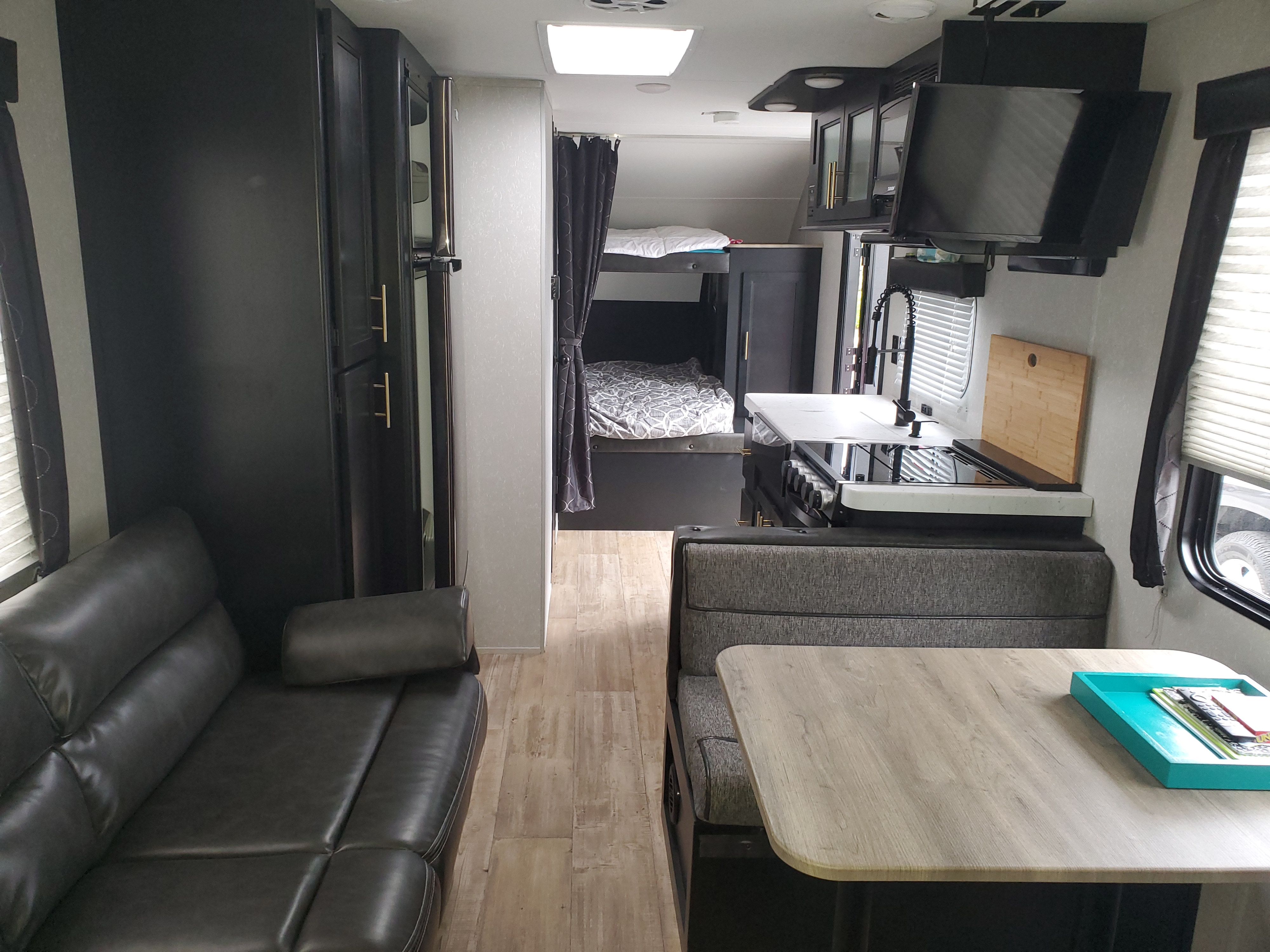 RV rental interior: living area with dark sofa, dinette, kitchen, and bunk beds in view.. Forest River Cherokee Grey Wolf 2021