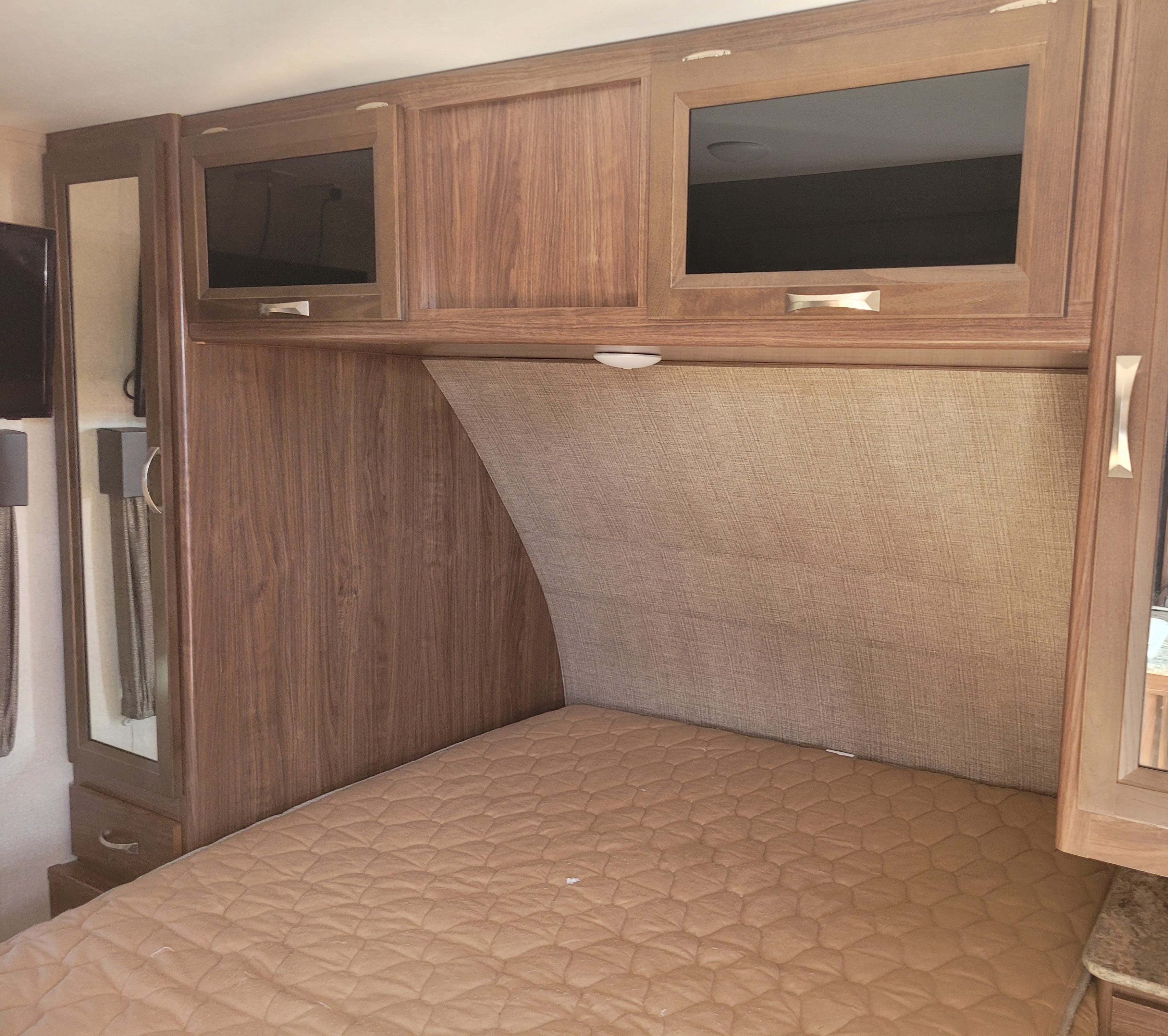 Cozy RV rental bedroom shows a bed with quilted pad, wood overhead cabinets, and mirrored closet.. Dutchmen Coleman 2017