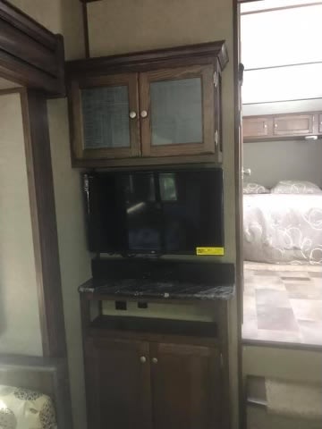 Interior of an RV rental showing the entertainment center with a TV and cabinets, plus a glimpse of the bedroom.. Keystone Sprinter 2016