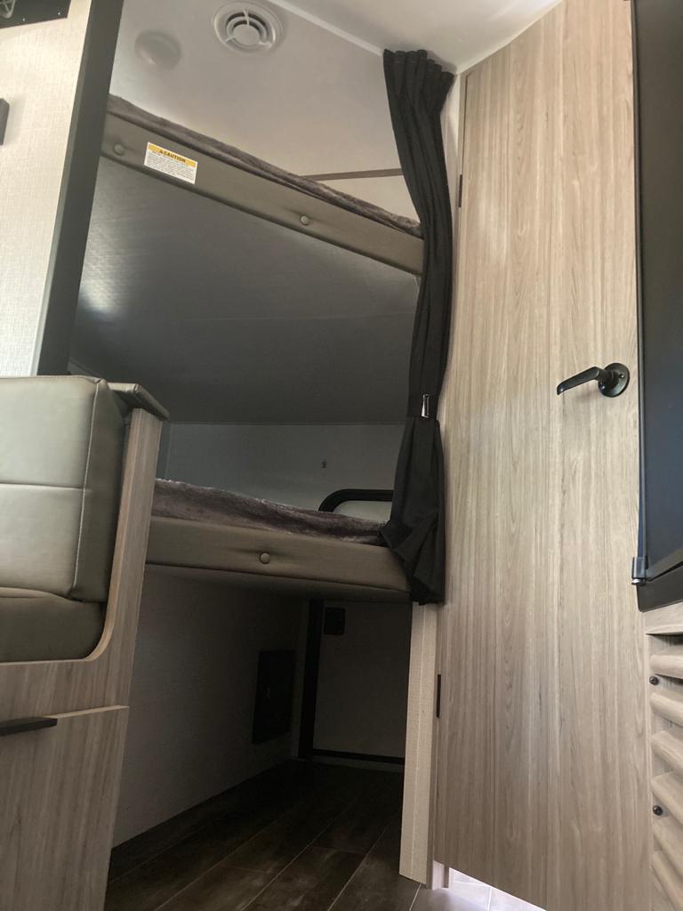 Cozy RV rental interior with bunk beds, perfect for family travel. A curtain provides privacy.. Keystone RV Passport SL 2021