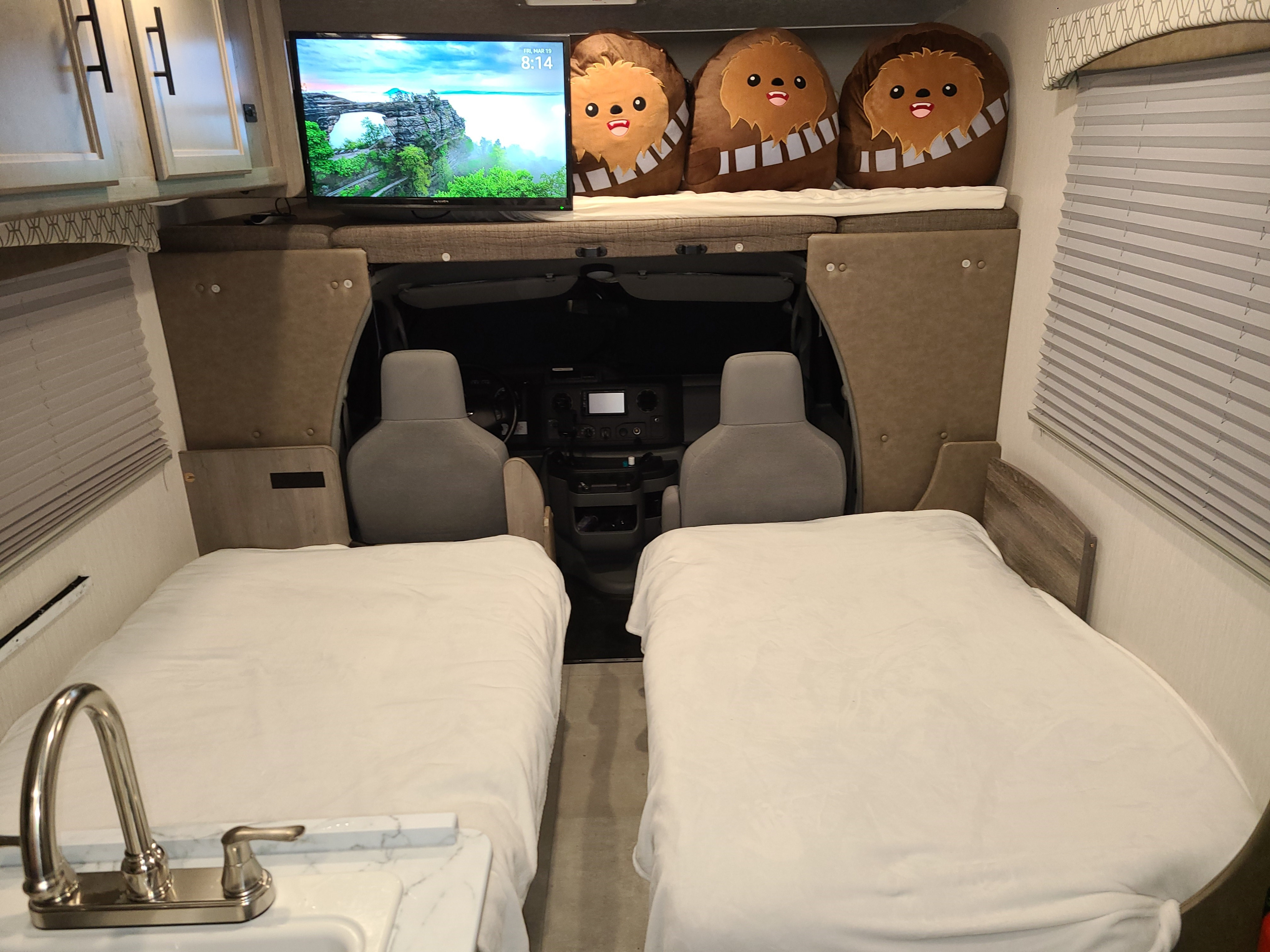 Inside an RV rental, showing two beds, a sink, and an overhead bunk with a TV and Chewbacca plushies near the cab.. Coachmen Freelander 2021