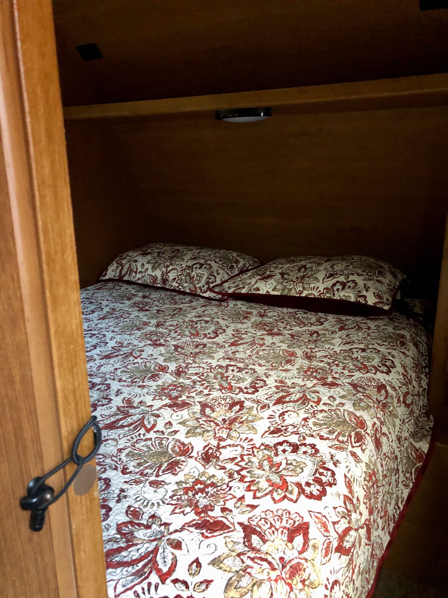 Compact RV rental sleeping area with floral bedding and cozy lighting, viewed through an open door.. Crossroads Sunset Trail 2015