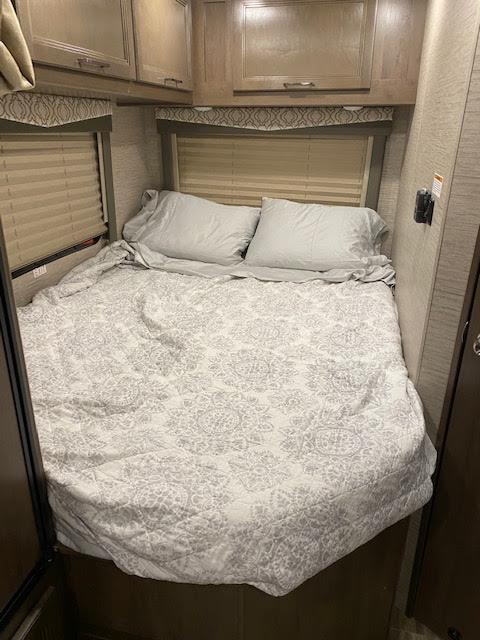 A comfortable RV rental bedroom interior with a patterned bedspread, pillows, and overhead cabinets.. Thor Motor Coach Freedom Elite 2021