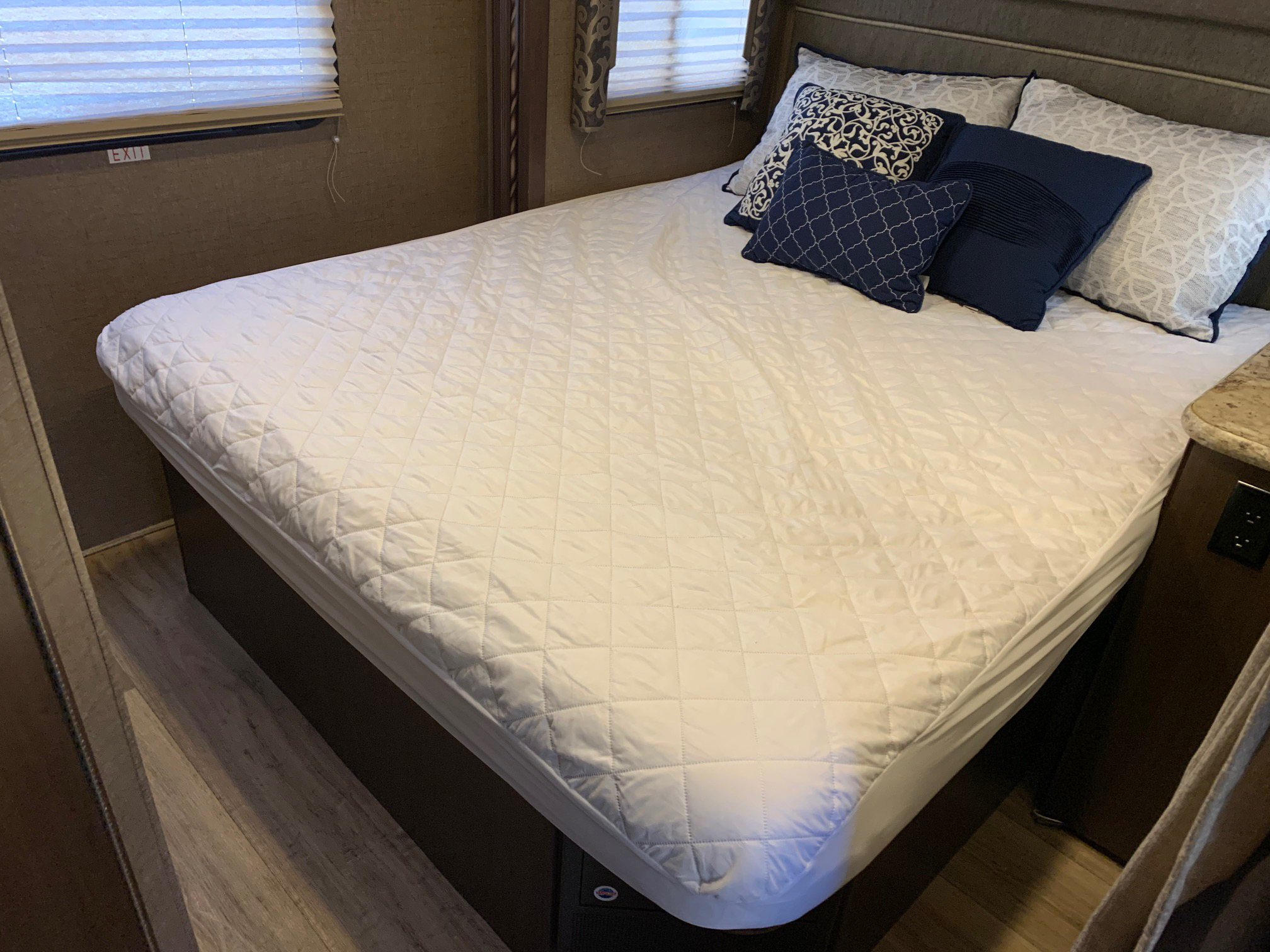 Plush bed in an RV rental bedroom with white quilted pad & navy/white pillows. Features a window & wood-look floor.. Thor Motor Coach Four Winds 2017