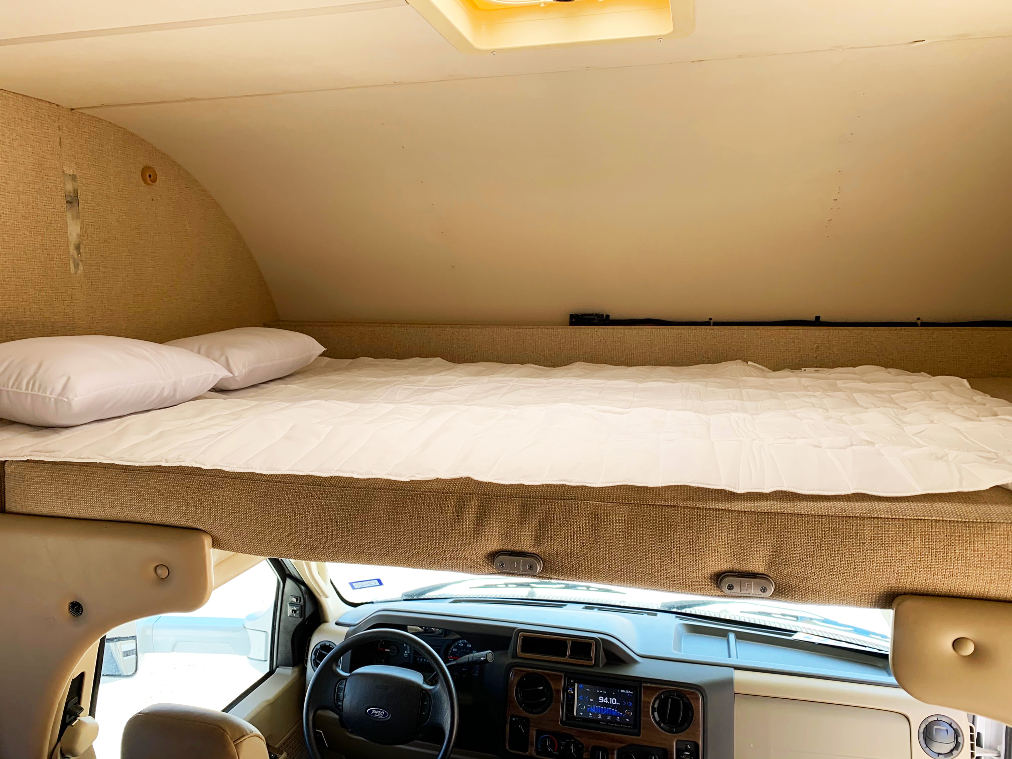 Inside an RV rental: a large, comfortable cab-over bed overlooks the driver's area and dashboard.. Thor Motor Coach Four Winds 2017