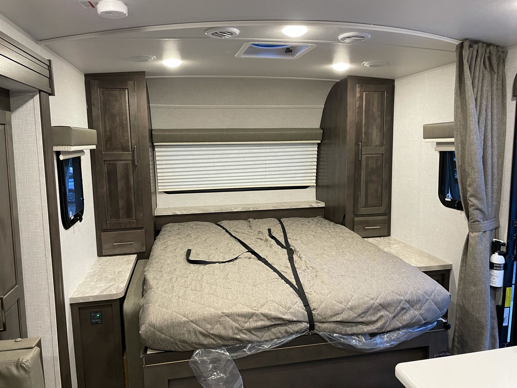 Inside an RV rental: a cozy bedroom with a neatly strapped bed, dark wood cabinets, and bright ceiling lights.. Forest River Mini-Lite 2021