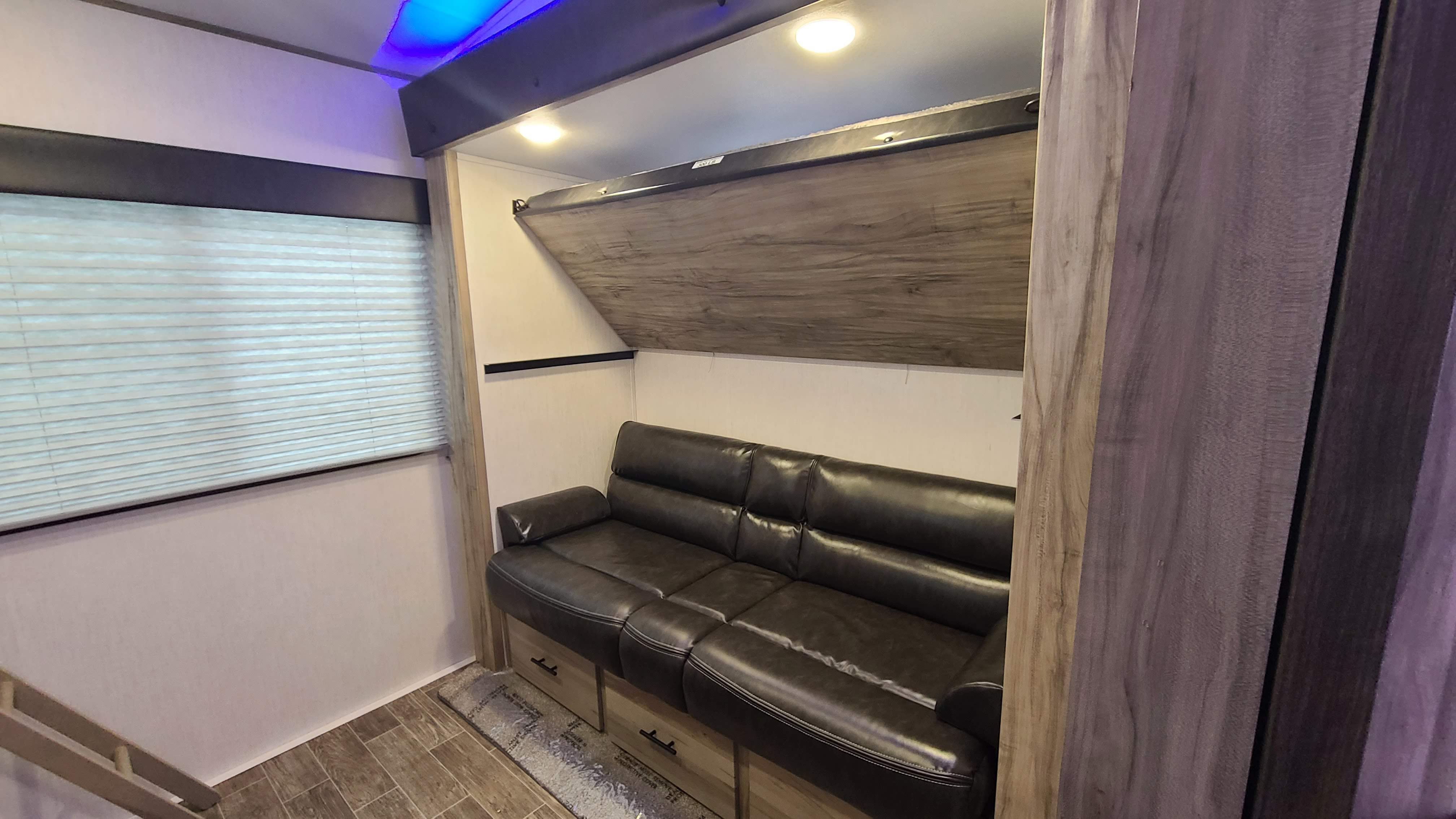 Cozy RV rental interior with dark sofa, fold-up bunk bed, and window with blinds. Perfect for a camper's relaxation.. Forest River Cherokee Grey Wolf 2021