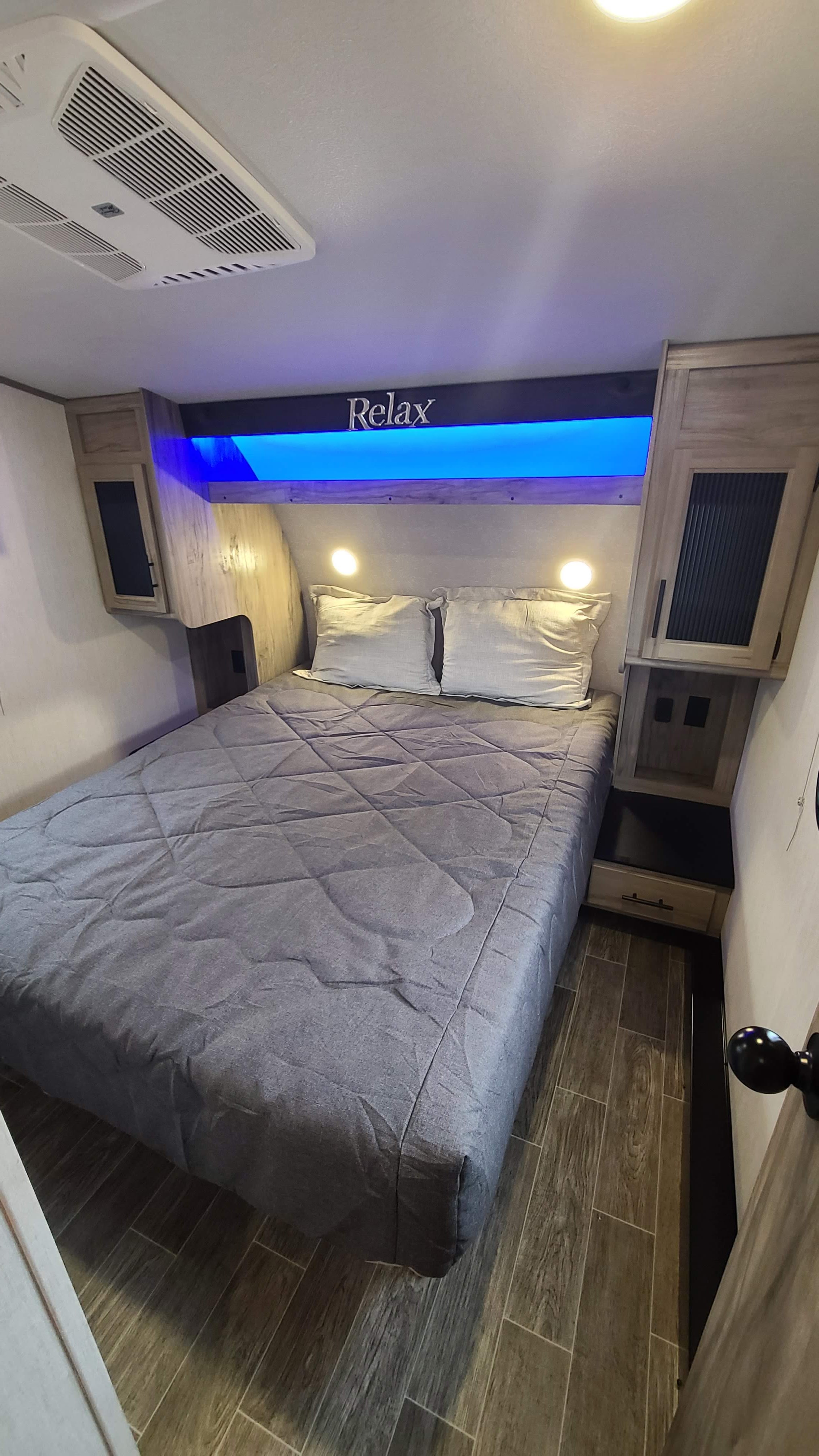 Spacious RV rental bedroom featuring a queen bed, 'Relax' sign with blue lights, AC, and bedside storage.. Forest River Cherokee Grey Wolf 2021