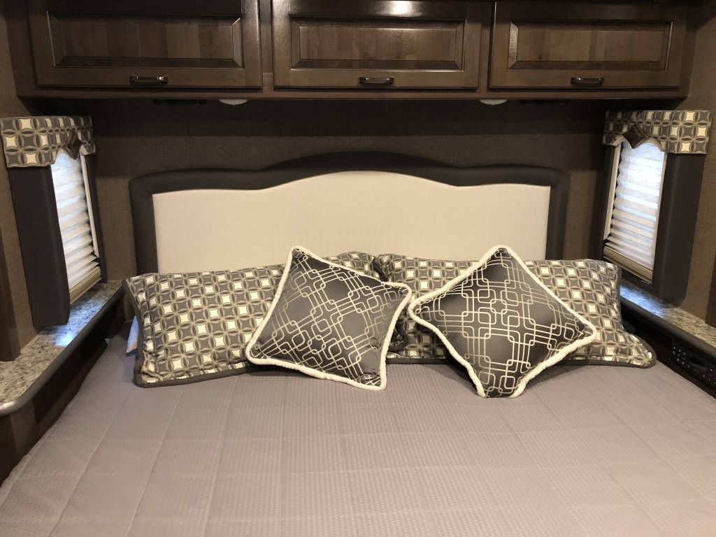 Plush, modern RV bedroom, ideal for your RV rental adventure. Relax with a stylish headboard and patterned pillows.. Thor Motor Coach Hurricane 2018