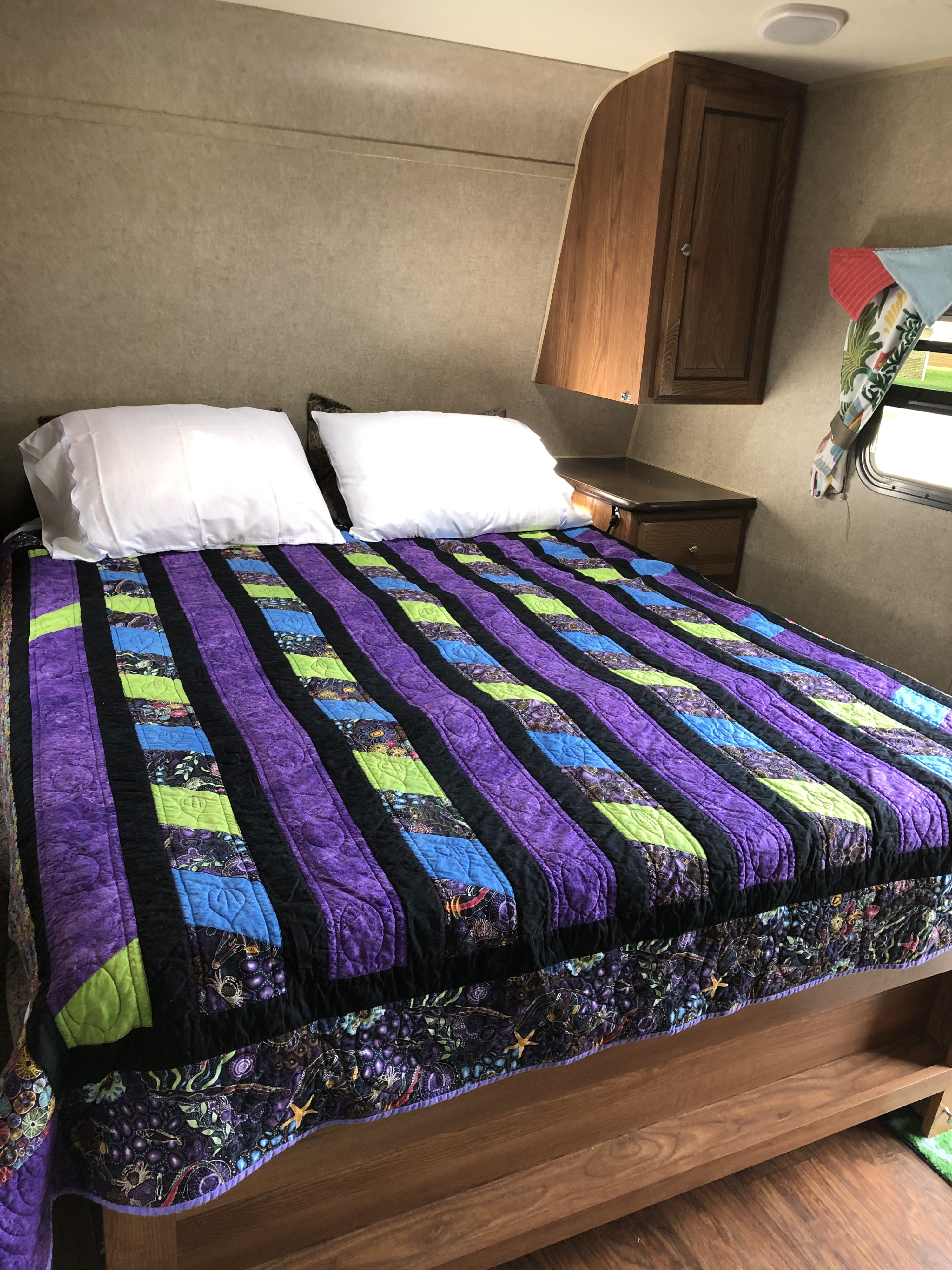 Cozy RV rental bedroom featuring a vibrant purple quilt, white pillows, and wooden cabinets, perfect for travel.. Forest River Rockwood Mini Lite 2015