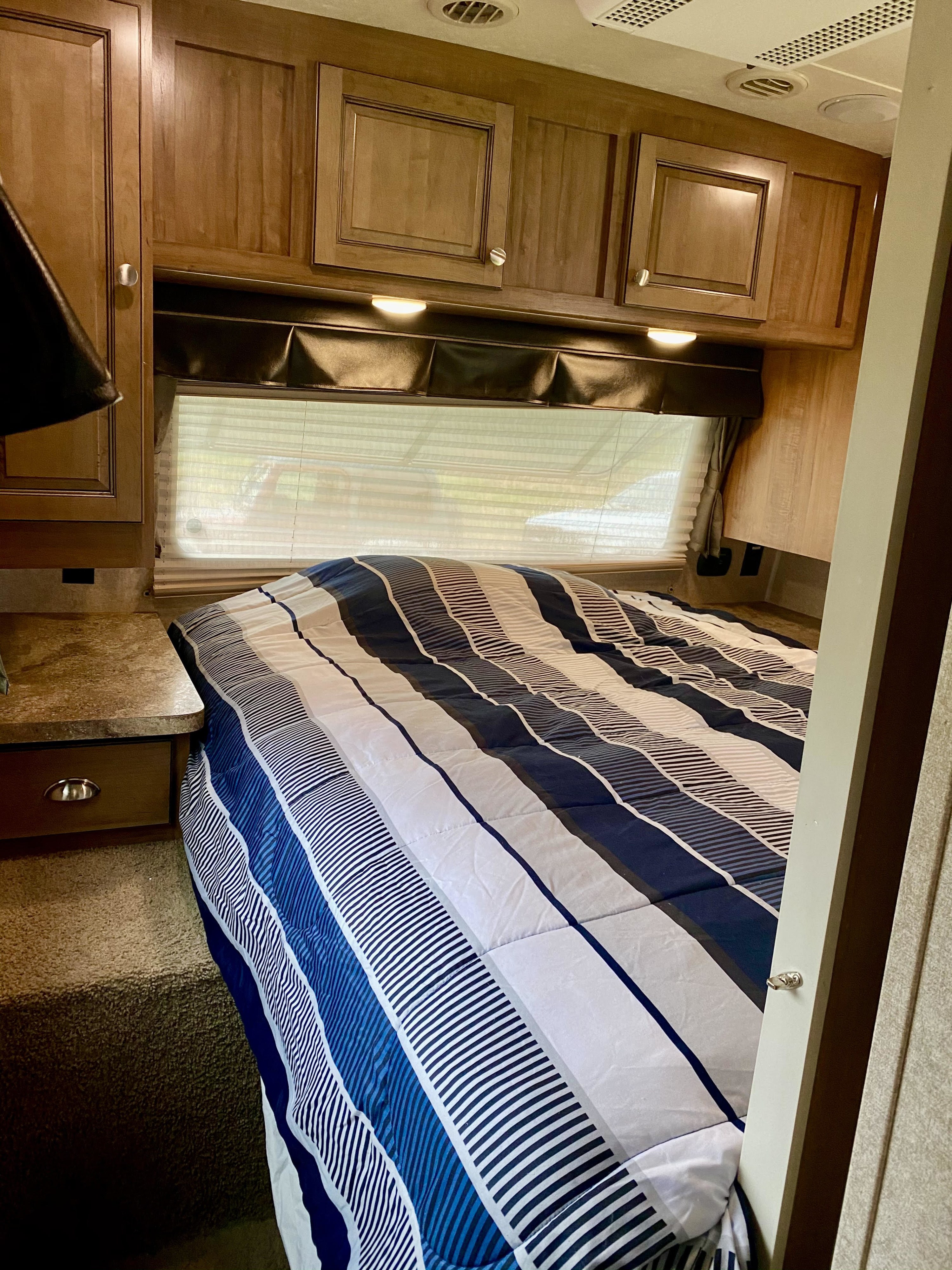 Cozy RV rental bedroom featuring a striped bed, wood cabinets, and a window with blinds for your next adventure.. Forest River Rockwood Signature Ultra 2016