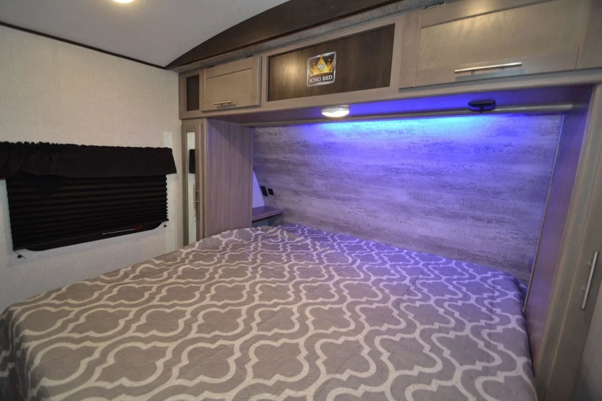 Cozy RV rental bedroom with a king bed, overhead storage, ambient blue lighting, and a large window.. Crossroads Other 2021