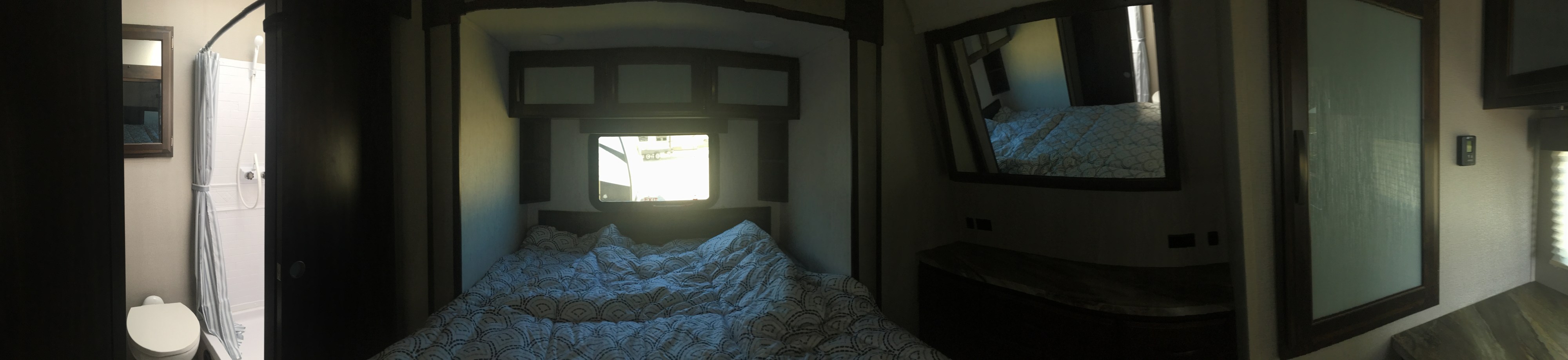 Compact RV rental interior featuring a cozy bedroom with a patterned bed, a private toilet and shower, and mirrored storage.. Grand Design Momentum 2020