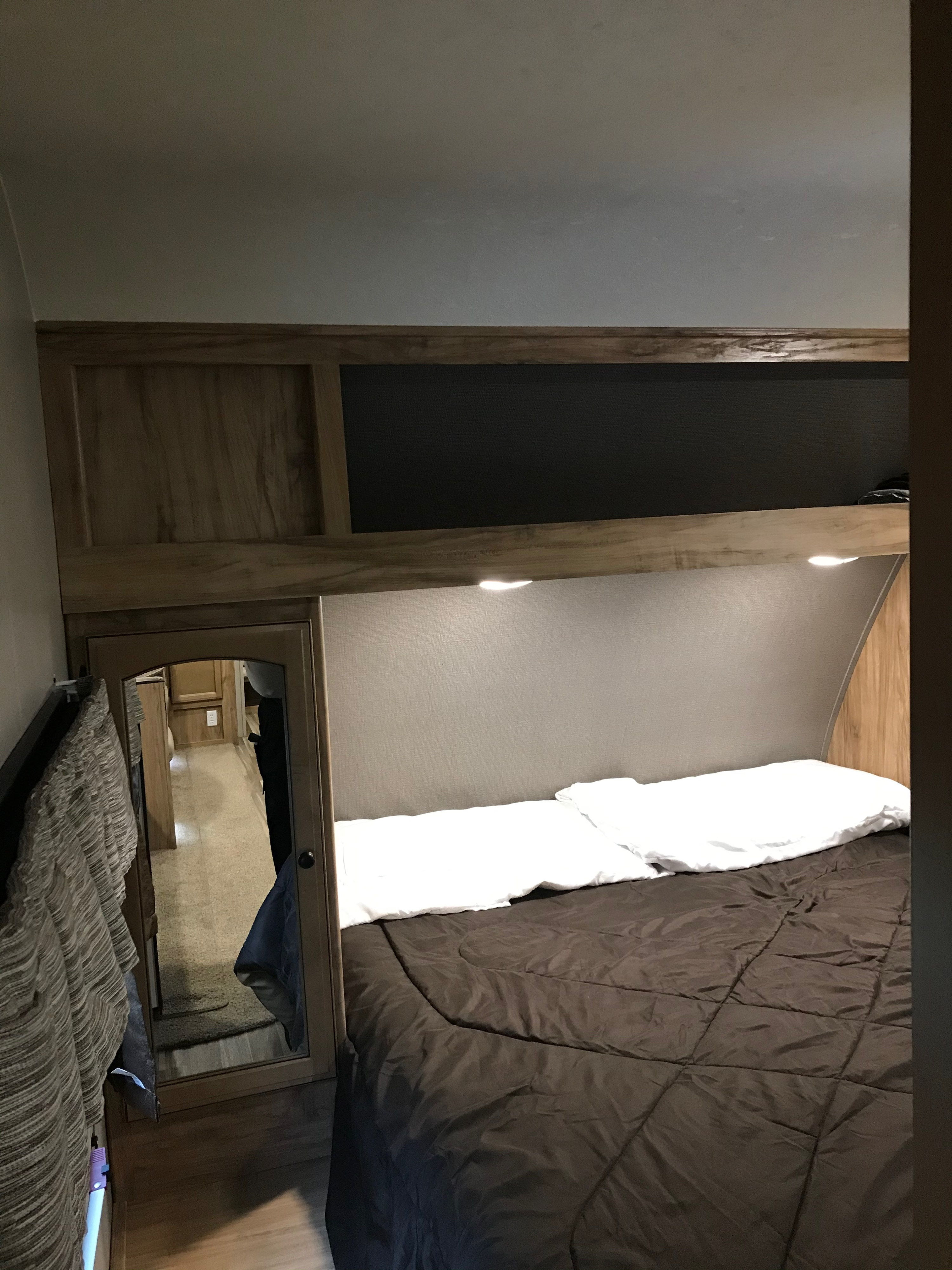 This RV rental bedroom features a comfortable bed, convenient overhead storage with lights, and a full-length mirror.. Coachmen Freedom Express 2018