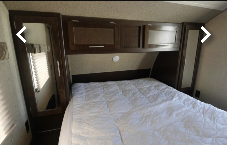 Inside an RV rental: a compact bedroom with a white quilted bed, overhead cabinets, and mirrored wardrobes.. Forest River Cherokee Grey Wolf - 29BH 2017