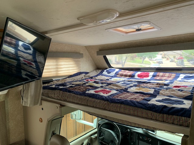 Inside an RV rental: a comfortable bunk bed with a patchwork quilt, TV, and scenic window view above the driver's cab.. Thor Chateau 2008