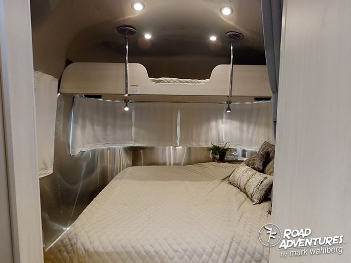 A compact RV rental bedroom with a large quilted bed, an upper bunk, ambient lighting, and sleek Airstream-style walls.. Airstream Flying Cloud 25FB Queen 2021