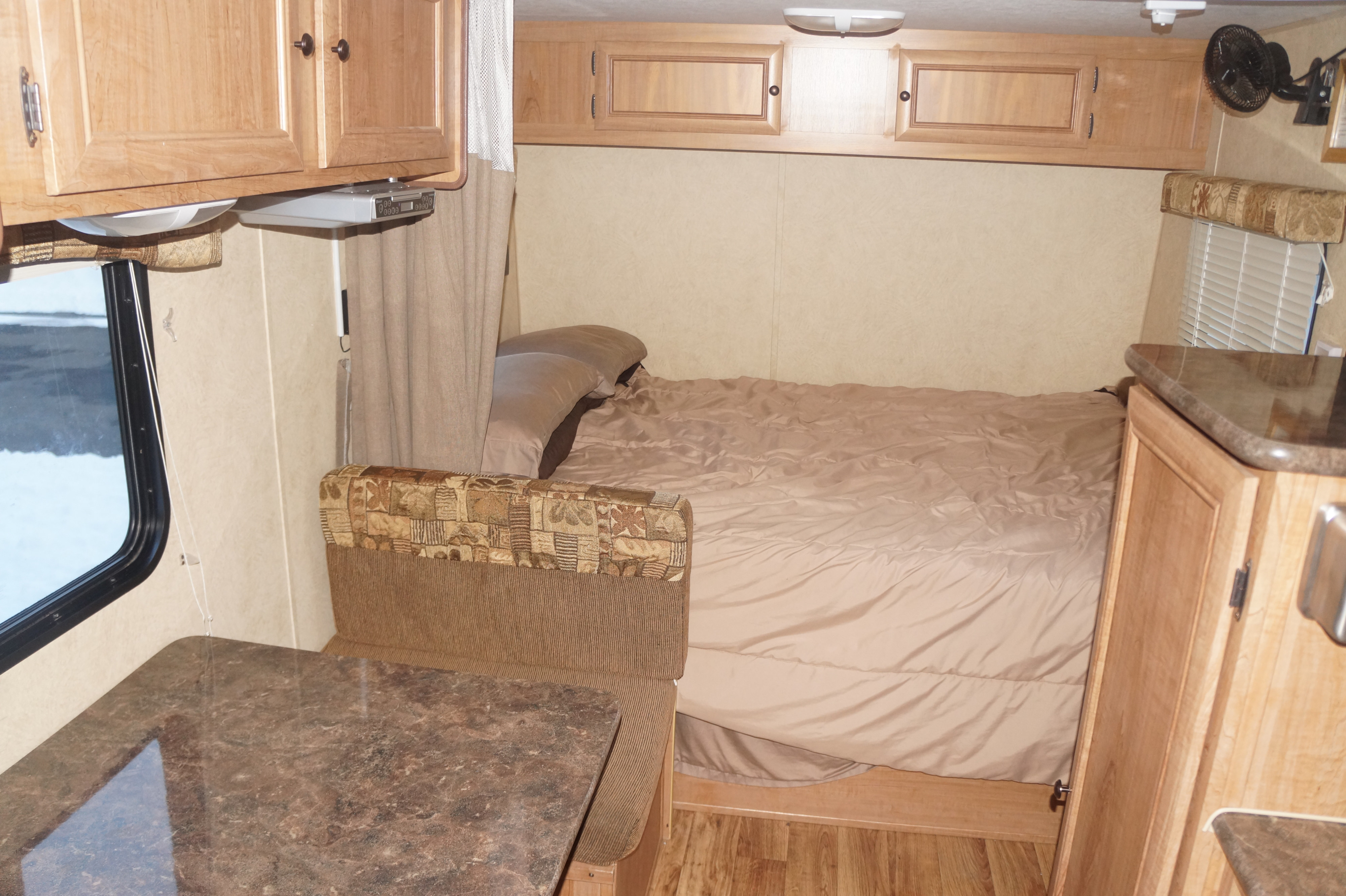 Inside a comfortable RV rental showing a bed, dinette table, and wood cabinets, ideal for road trips.. Skyline Nomad 2013