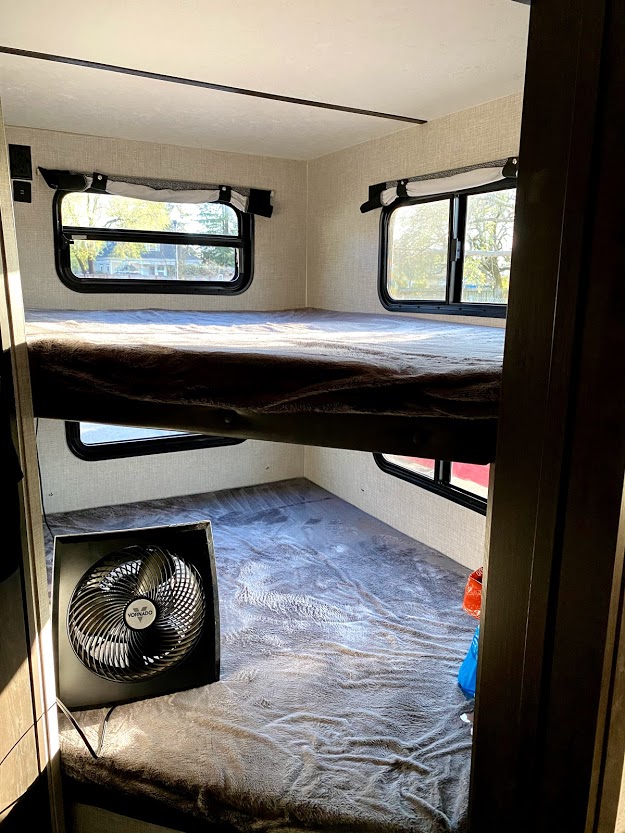 Cozy RV rental bunk beds, stacked with windows revealing outdoor views and a fan on the lower bed.. Keystone Bullet 2021