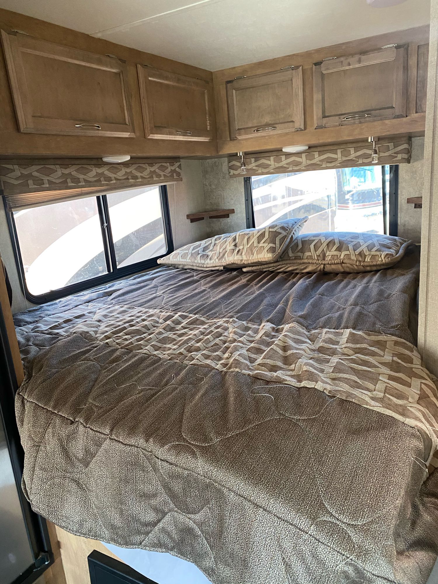 Step into comfort with this RV rental's cozy bedroom, featuring a patterned bed, overhead cabinets, and bright windows.. Gulf Stream Conquest 2018