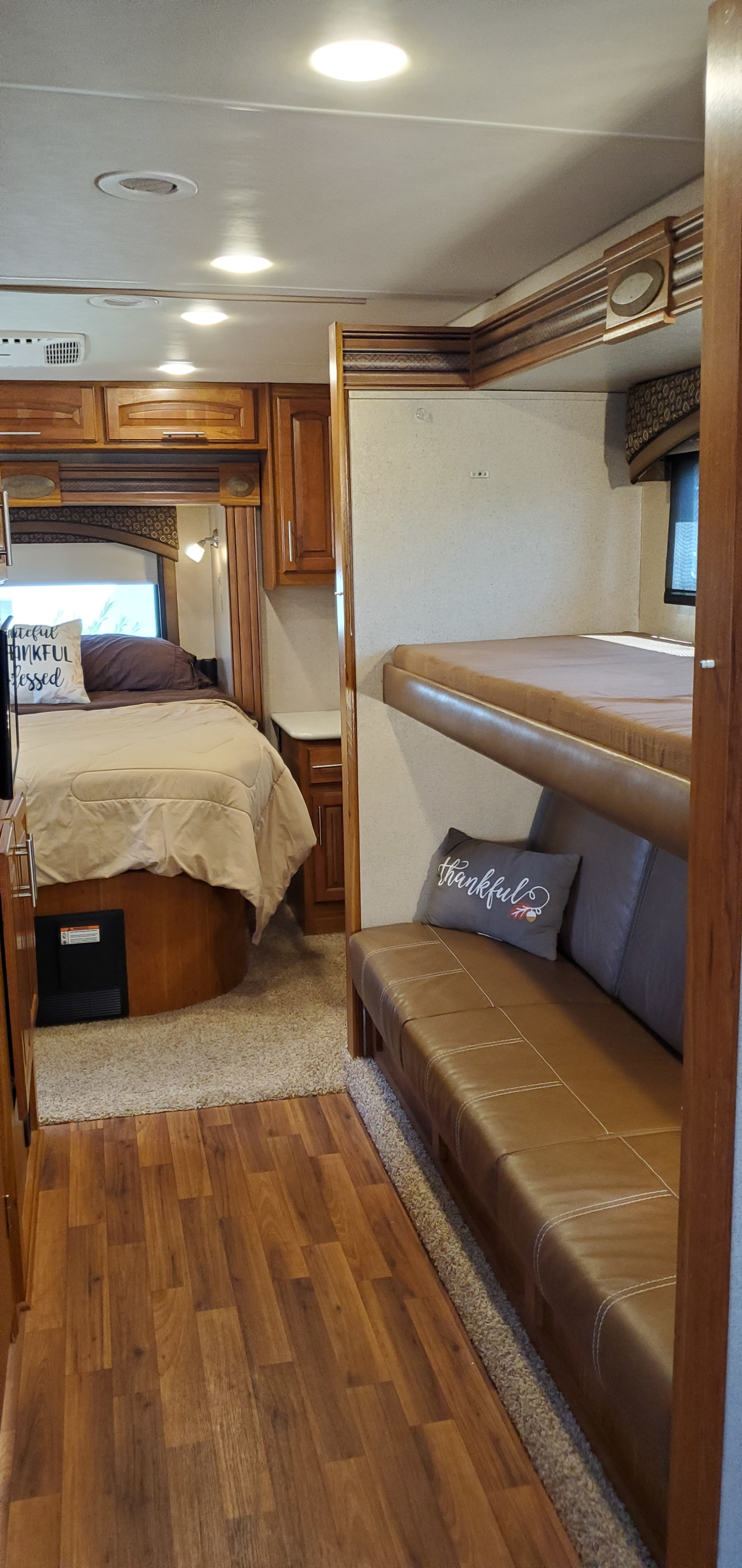 Cozy RV rental interior featuring a comfortable bedroom, bunk beds, wood cabinets, and combined wood/carpet flooring.. Jayco Precept 2016
