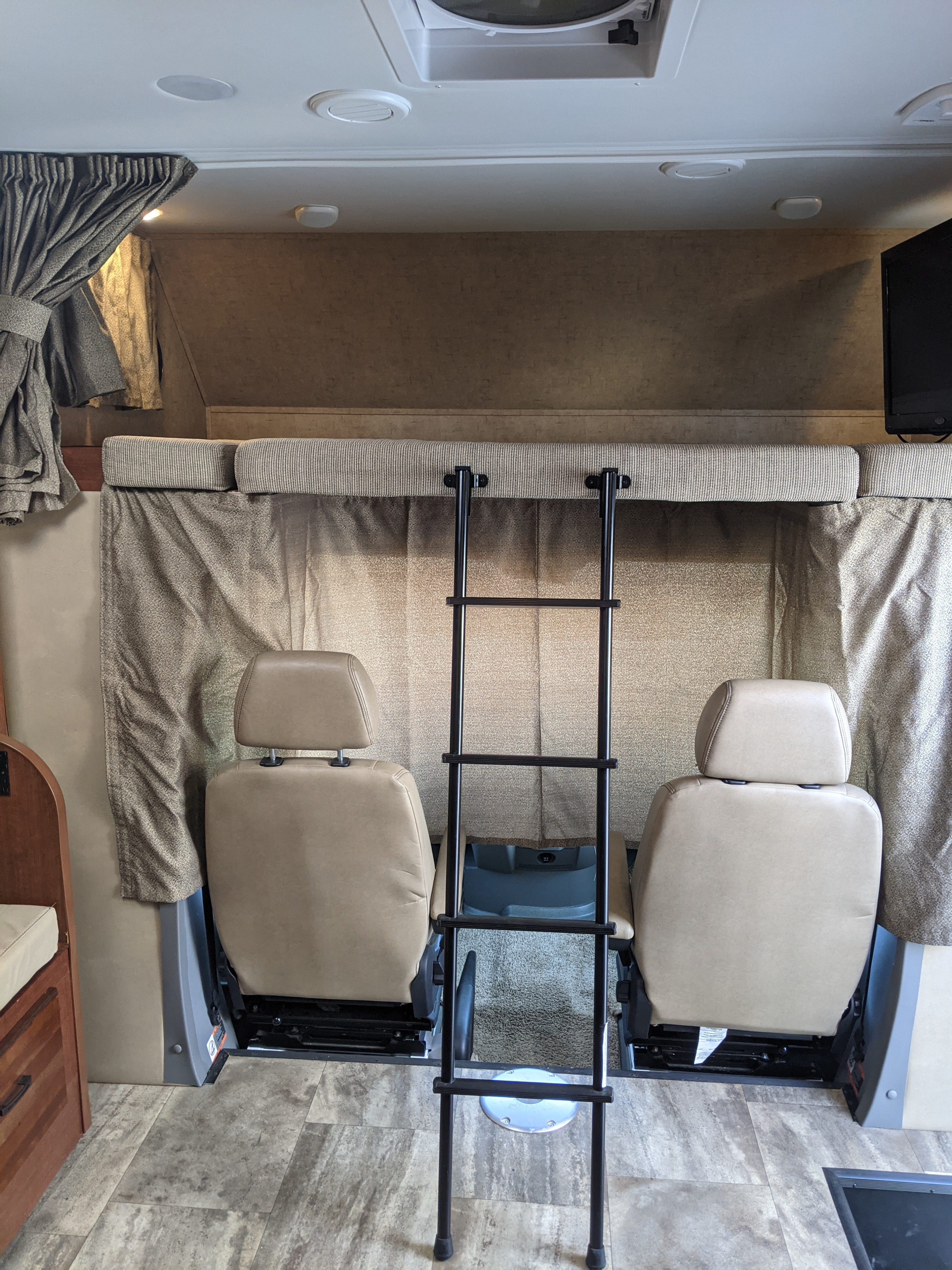 Spacious RV rental interior featuring front seats, an overhead bunk with ladder, curtains, and vinyl flooring.. Forest River Sunseeker 2016