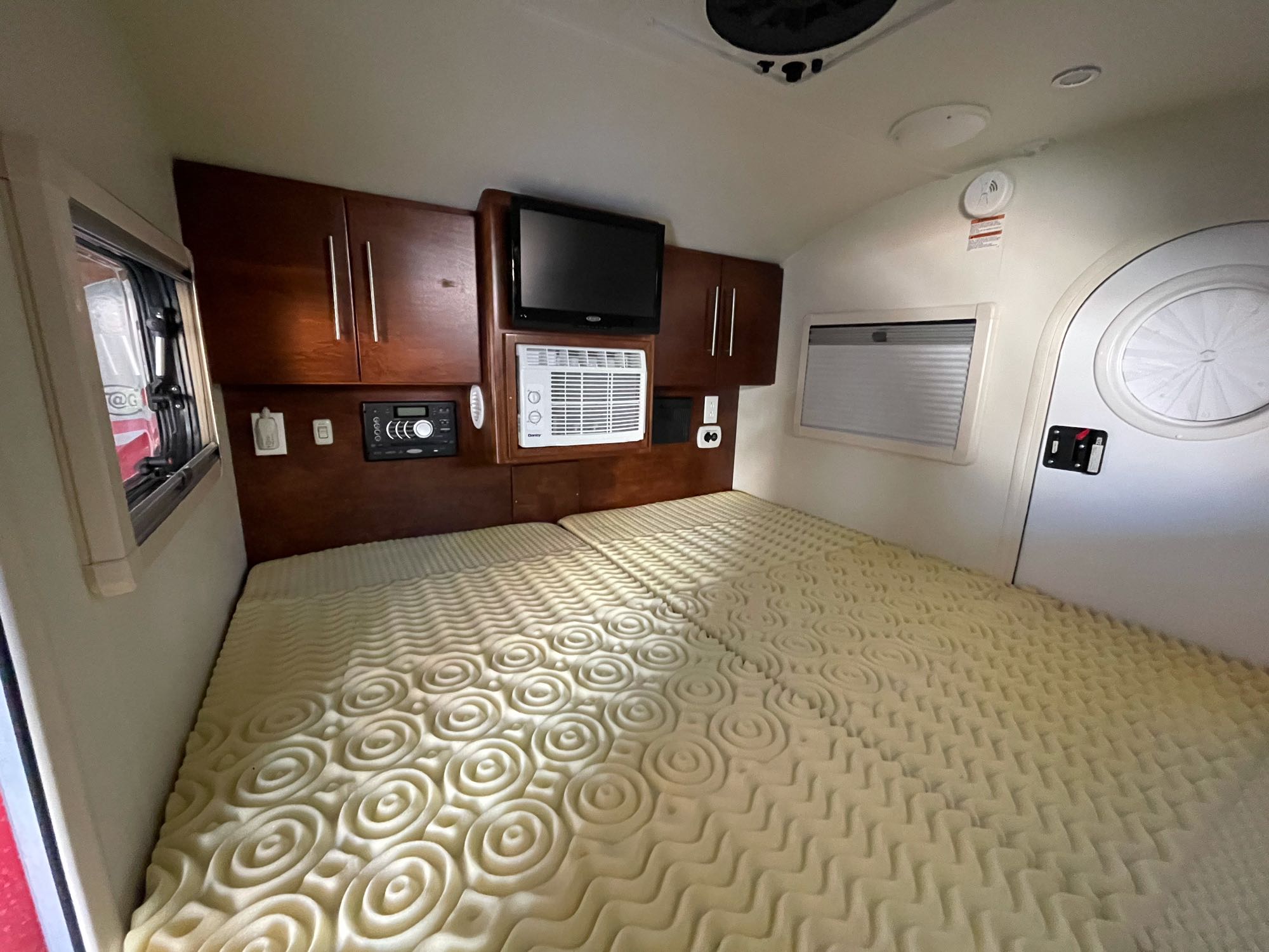 Spacious RV rental bedroom showcasing a bed with foam topper, TV, AC, and wood cabinets.. T@G XL 2017