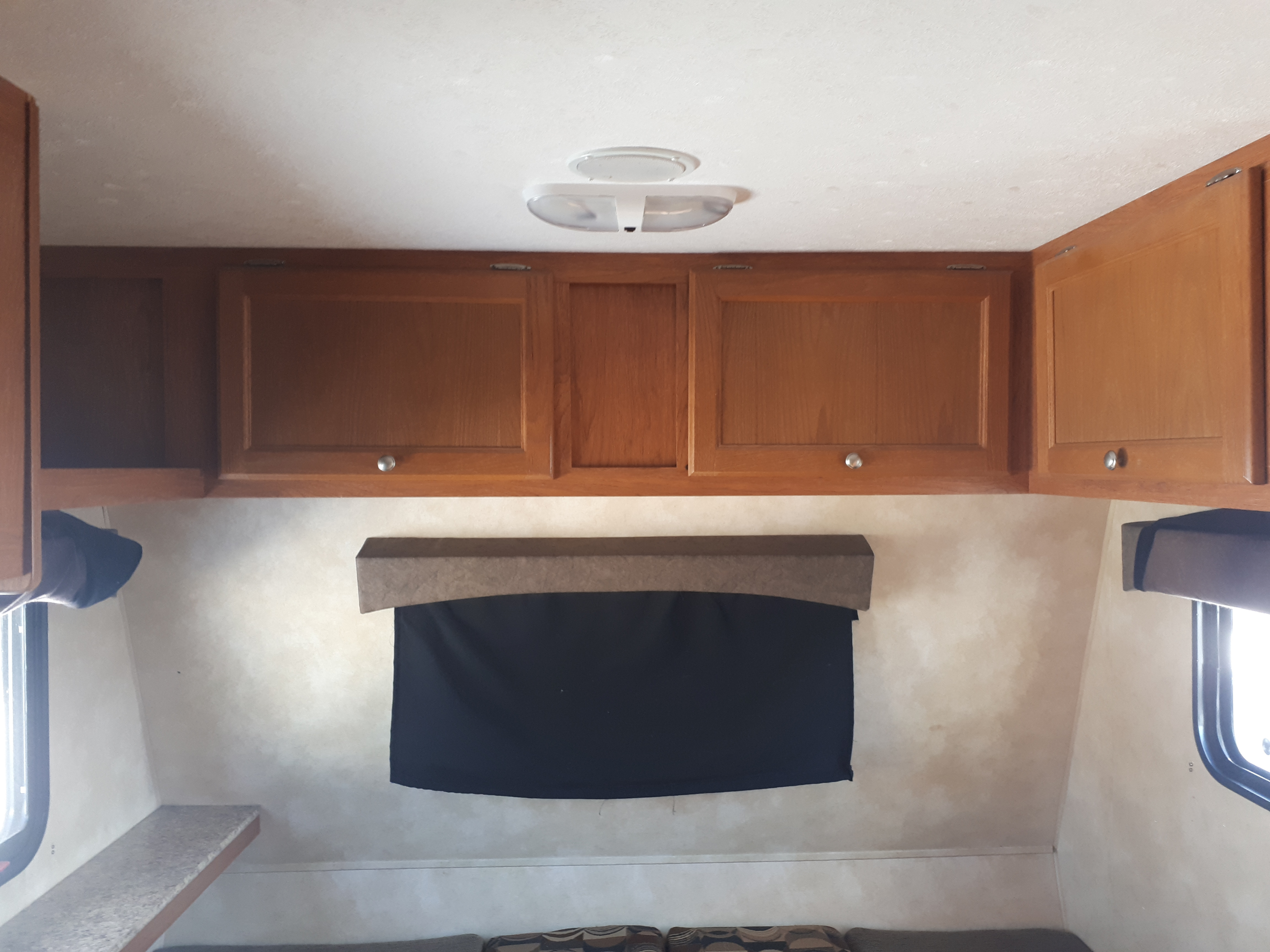 Light wooden overhead cabinets, ceiling light, and a black-out window shade in this compact RV rental interior.. Coachmen Clipper 2013