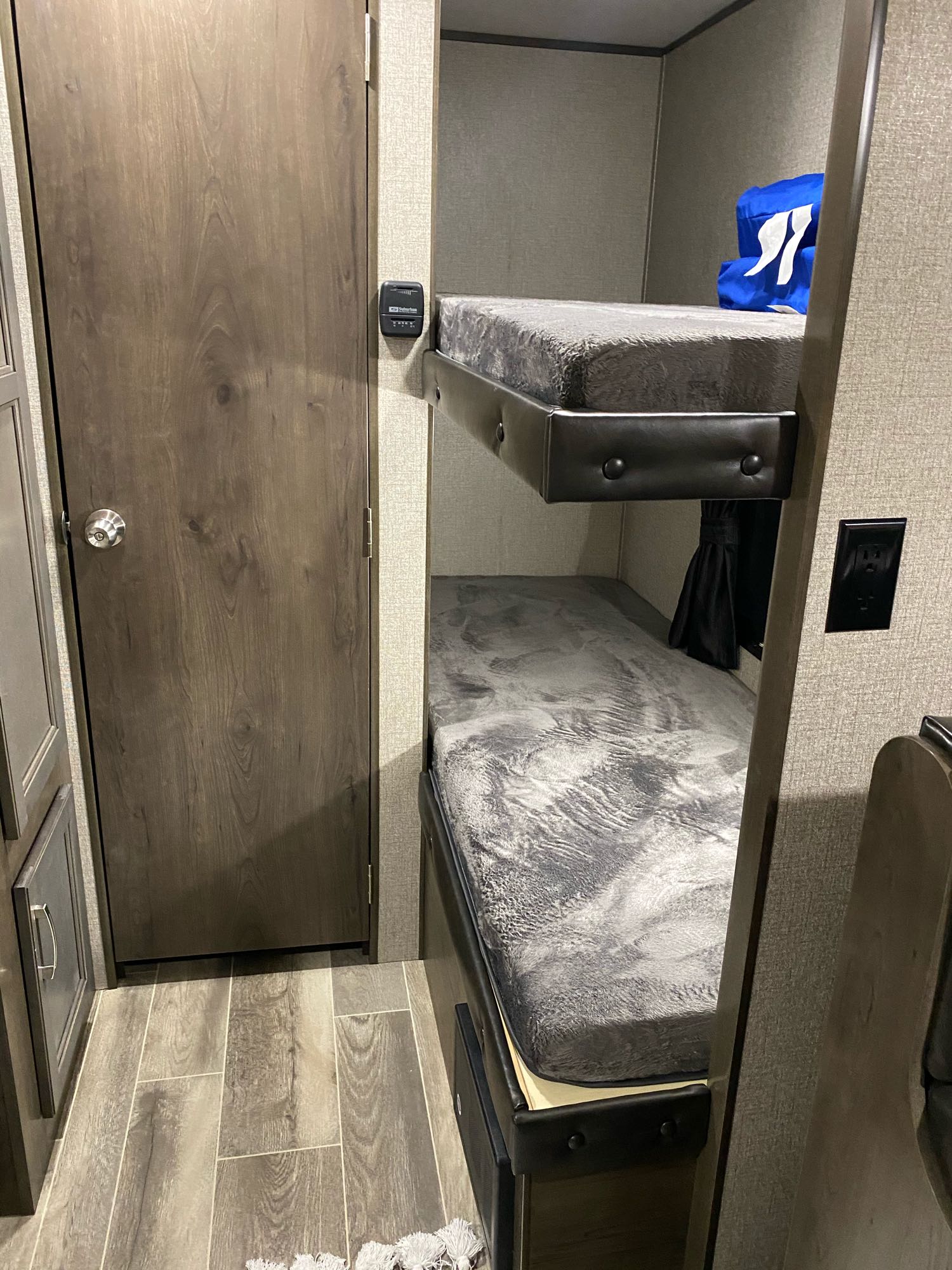 Inside this RV rental: a set of stacked bunk beds with grey bedding, a wooden door, and wood-look flooring.. Jayco Jay Flight Swift 2021