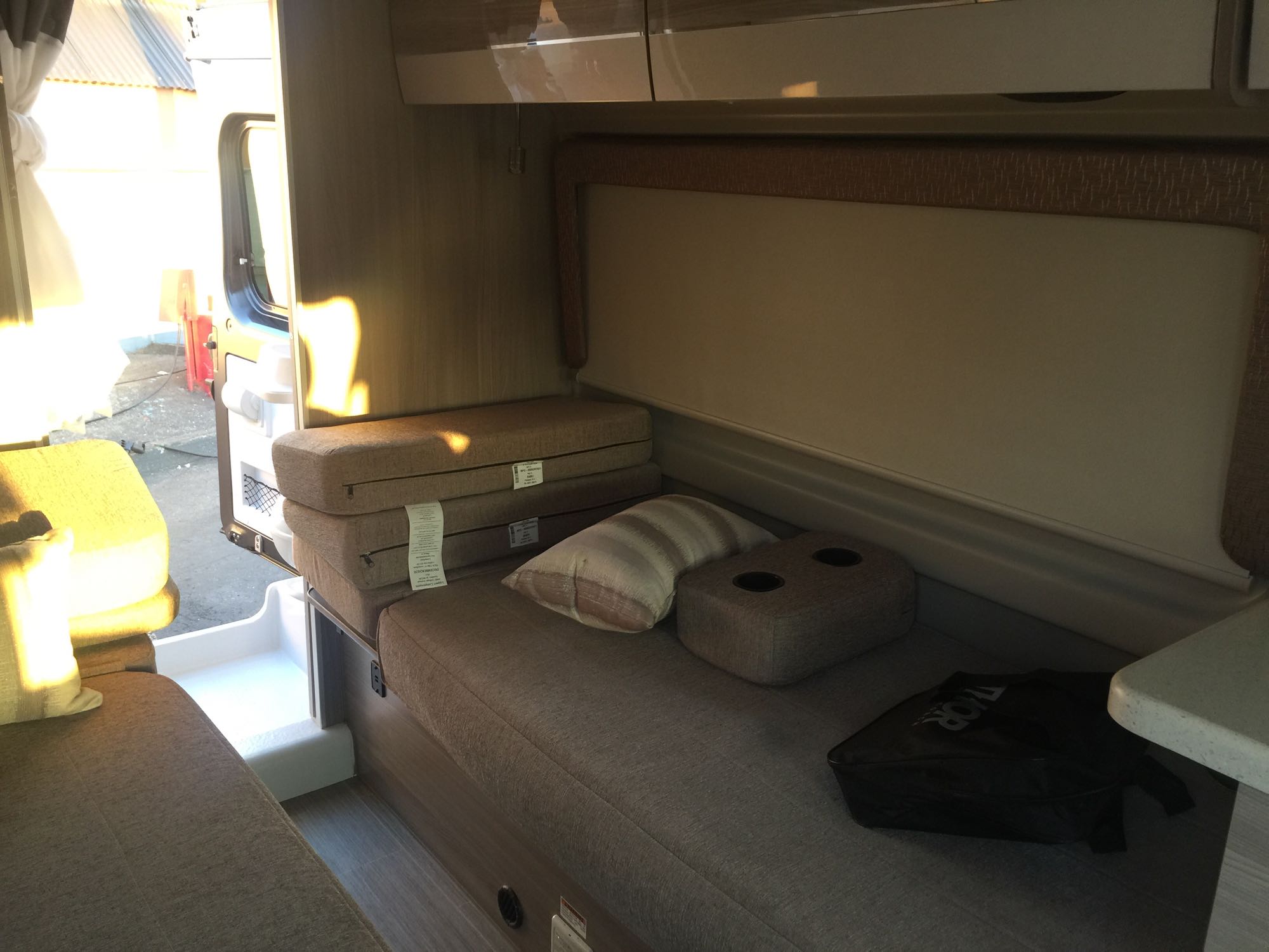 Inside a bright RV rental: compact living space with comfortable bench seating, foldable cushions, and an open side door.. Thor Sequence 2021